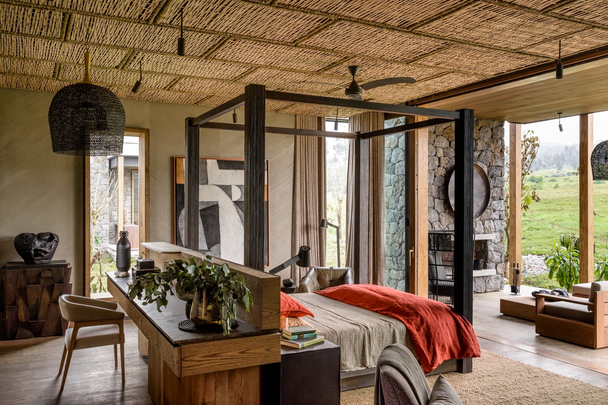 Four-poster bed, desk and stone fireplace under a woven ceiling