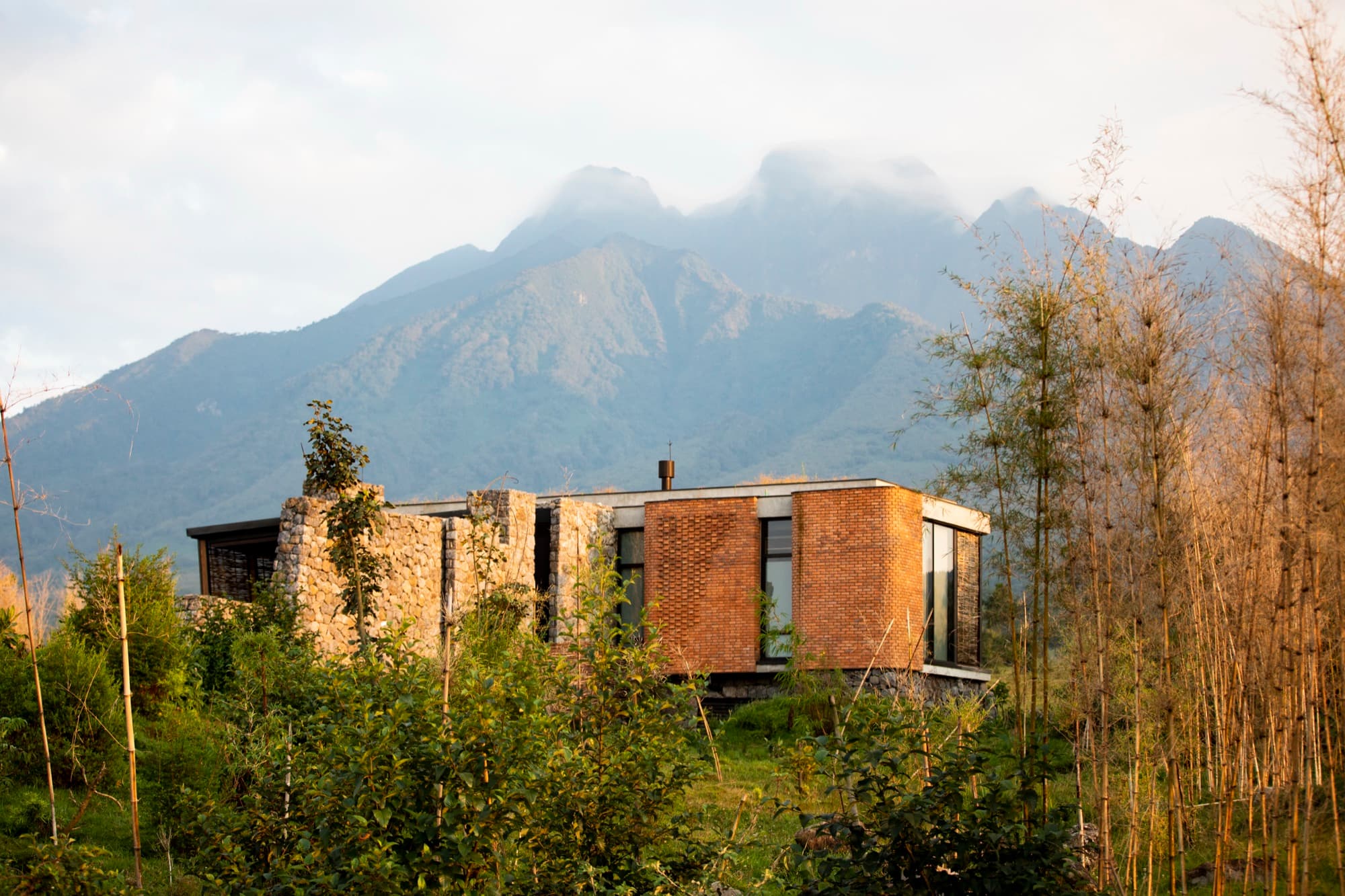 A suite of volcanic stone and red brick among young trees, volcanoes behind