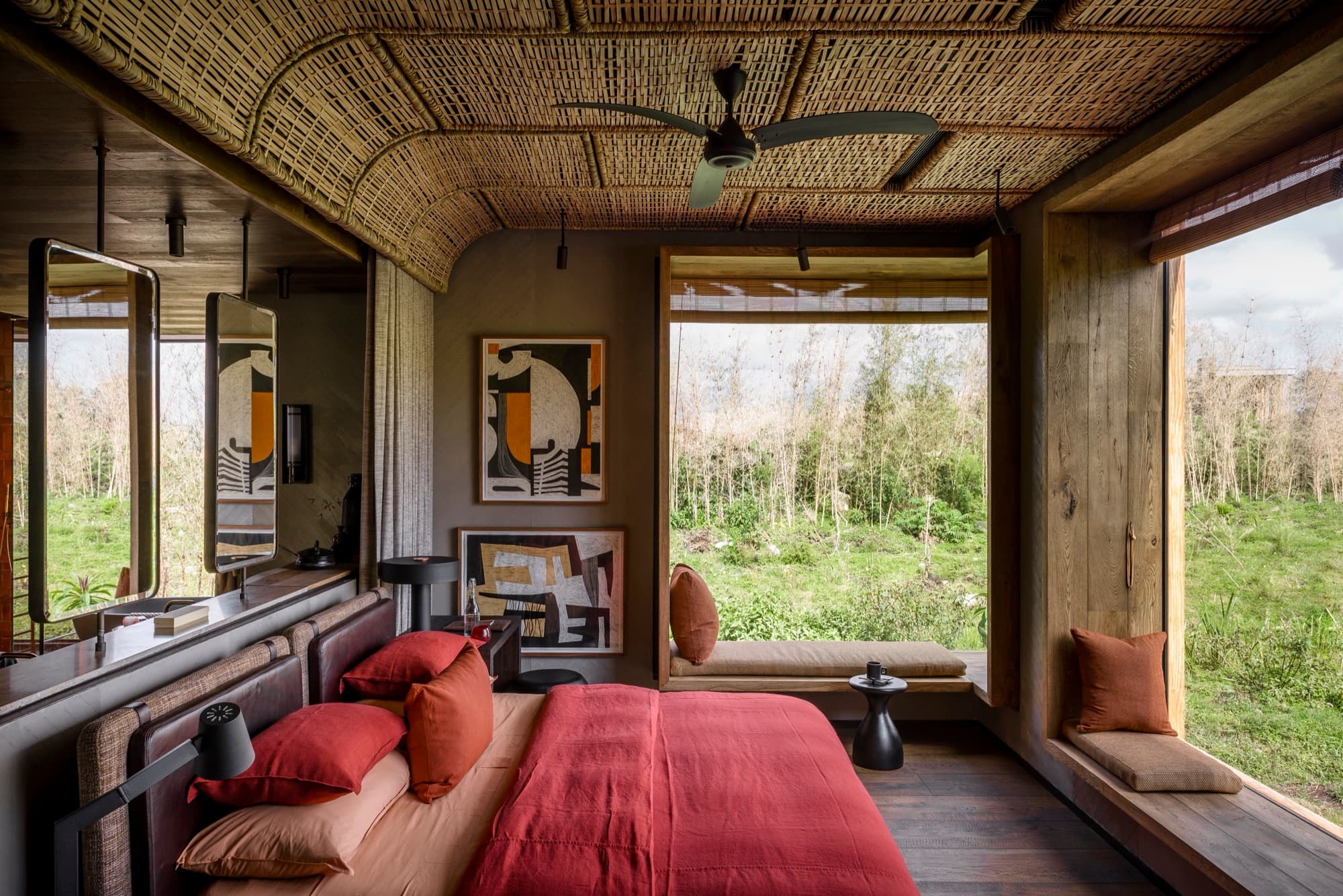 Suite with a woven ceiling, red bedding and a wide window onto the fields