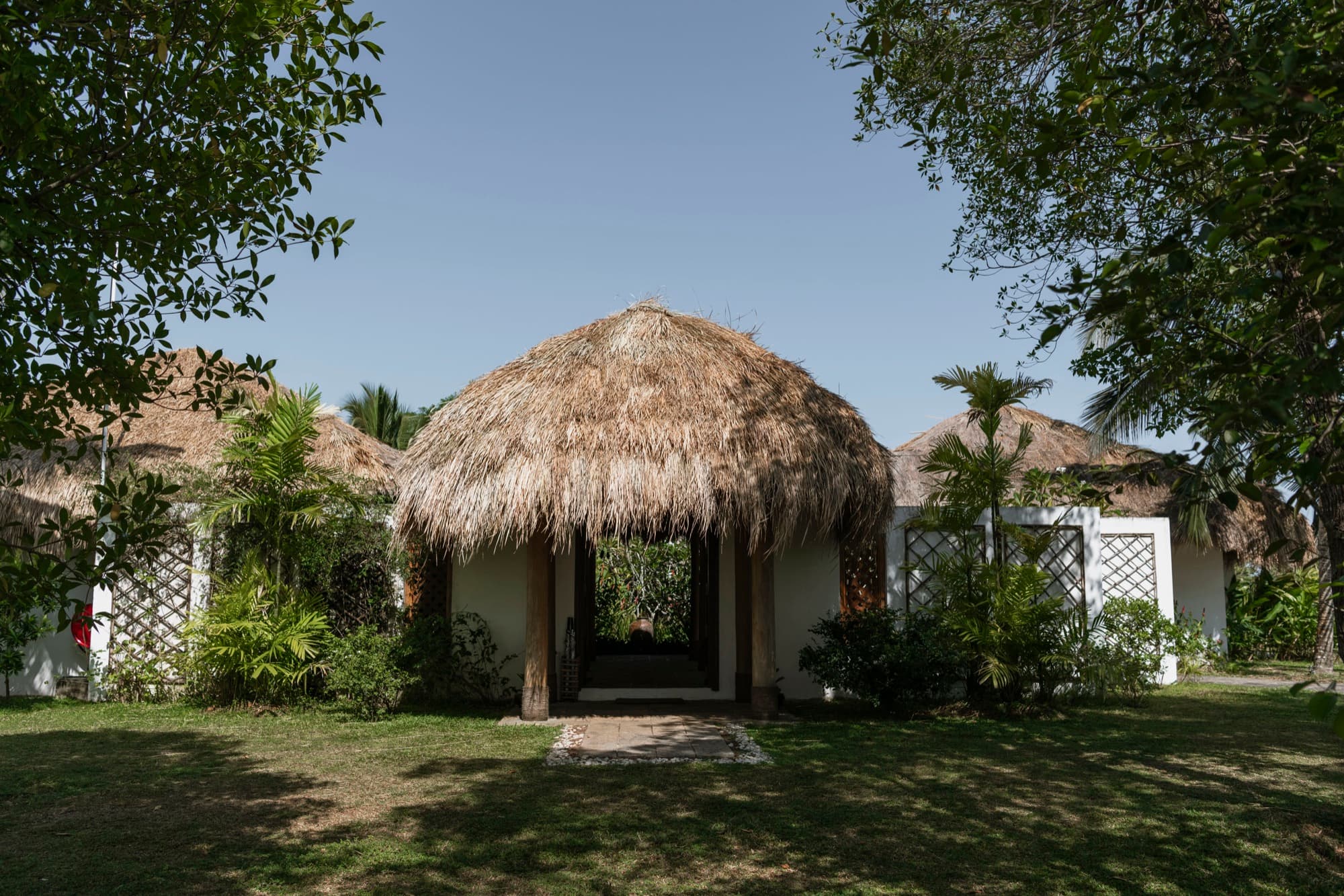 Whitewashed lodge with a thatched entrance porch surrounded by lawn and palms