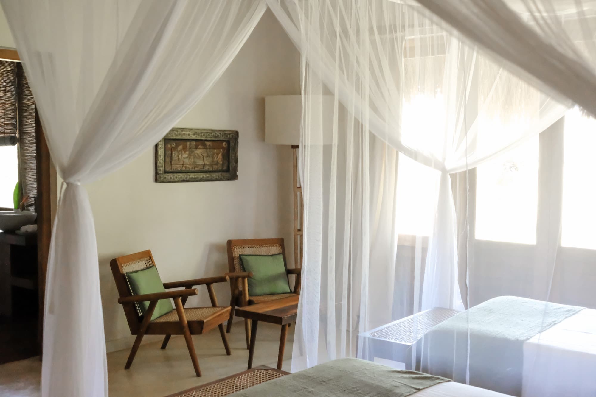 Bedroom with white mosquito-net canopies over twin beds and cane armchairs