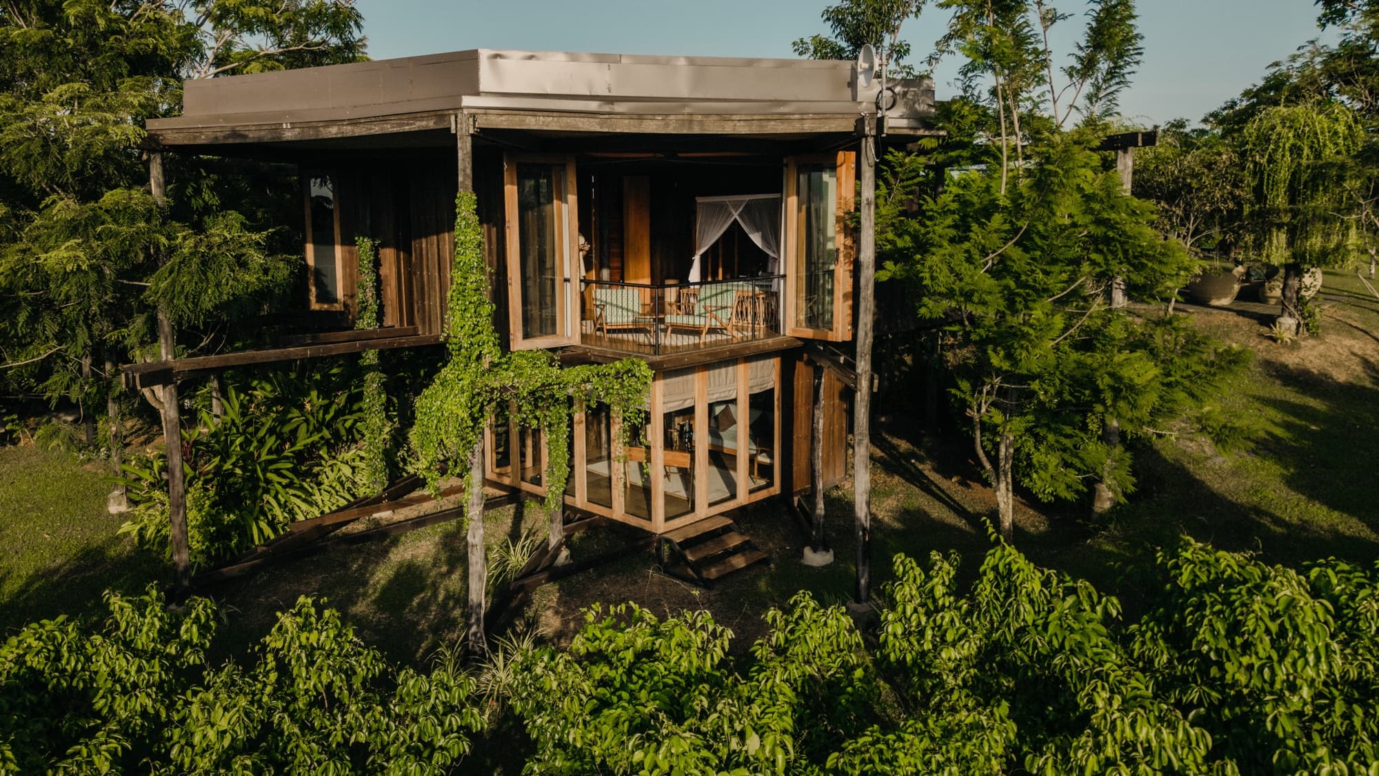 Two-storey timber suite raised on stilts among the trees at golden hour