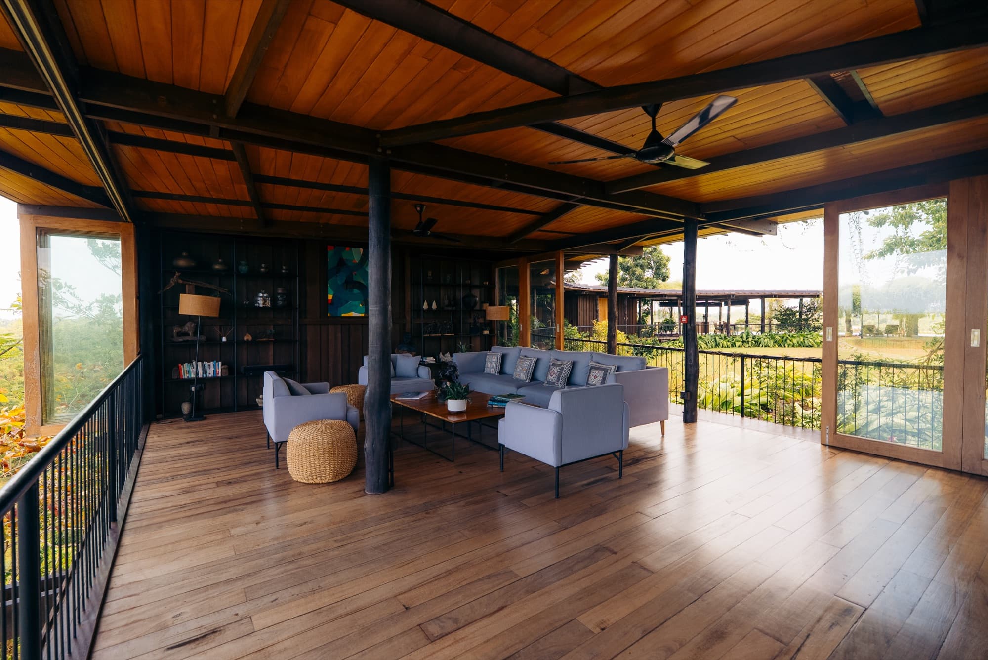 Open-sided lounge with a grey sofa and timber ceiling opening onto the deck and view
