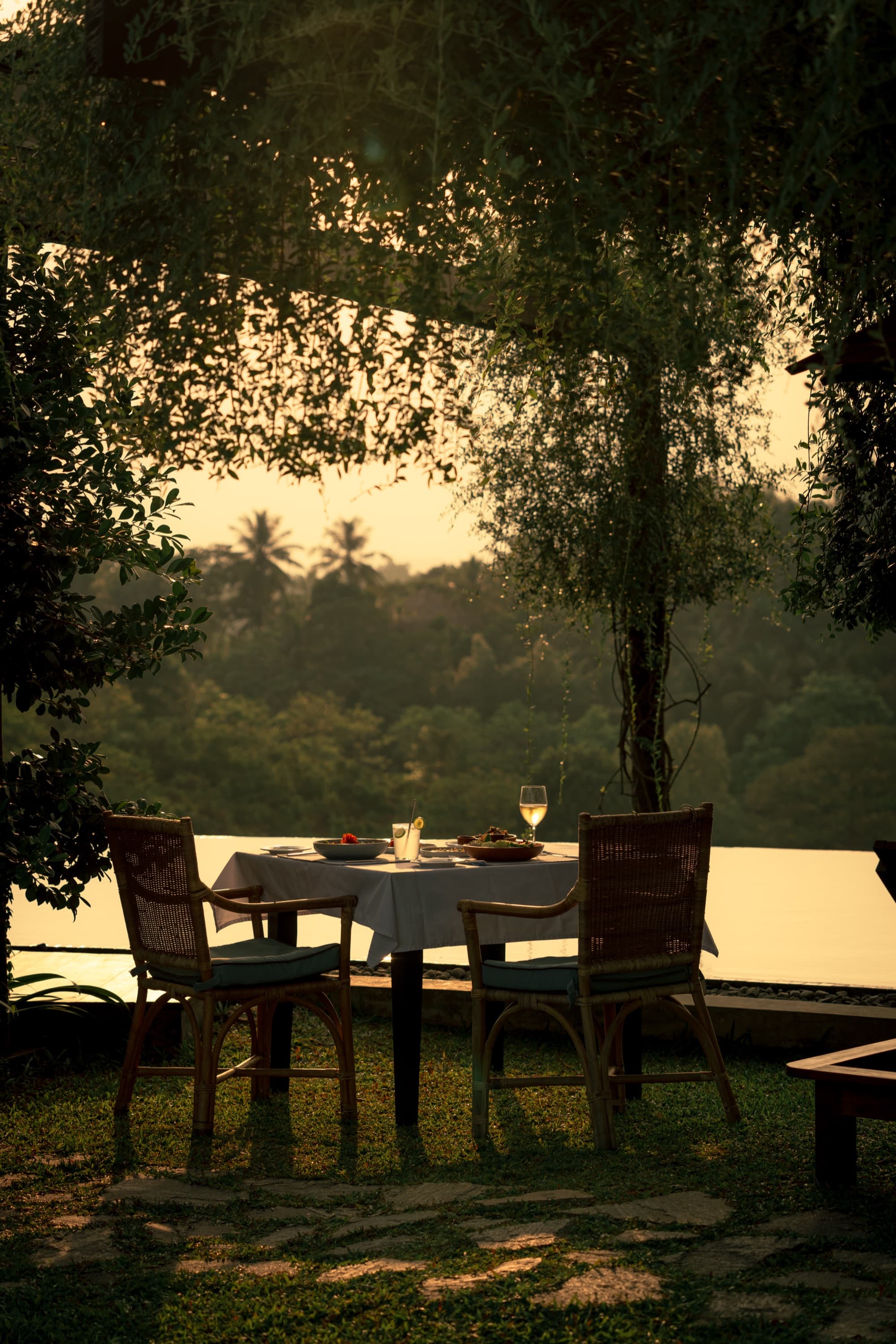 Private table for two set on the lawn under trees at sunset