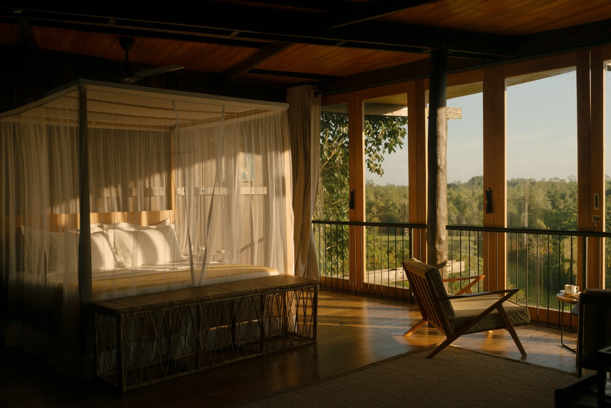 King room with a draped canopy bed and a lounge chair by windows onto the hills at sunset