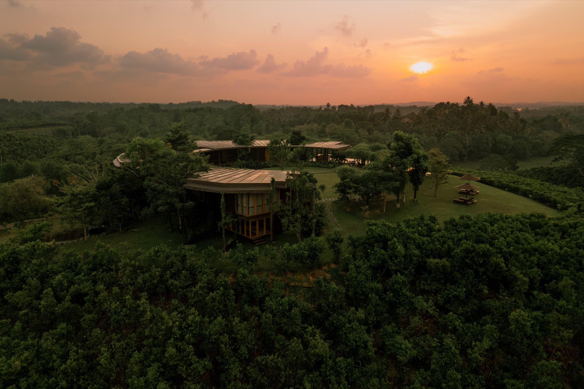 The roundhouse amid jungle and plantation under an orange sunset sky, seen from the air