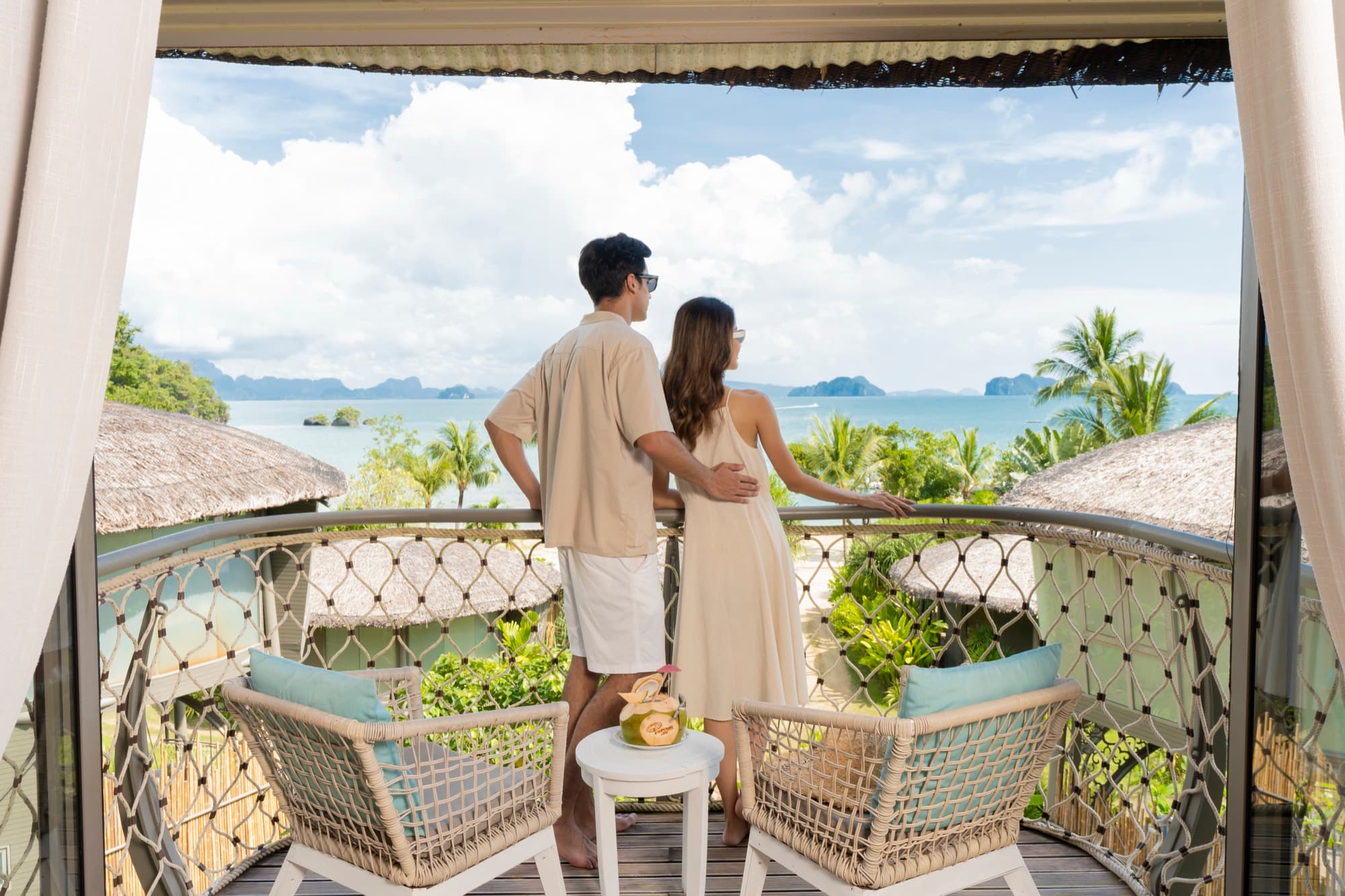 Villa balcony with two rattan chairs looking over thatched roofs towards the limestone islands of the bay