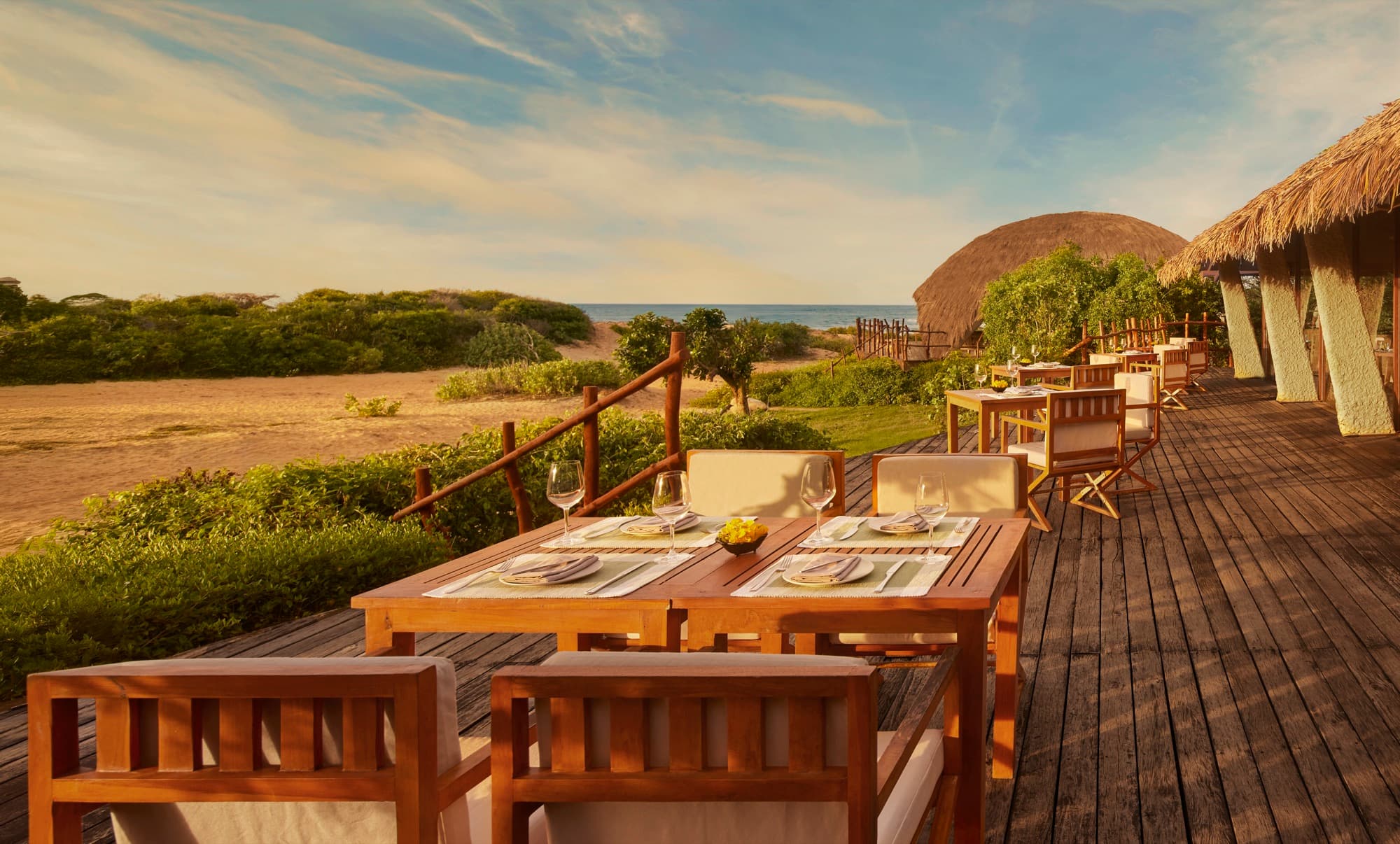 Dining tables on the wooden deck of Basses, with the bush and the domed buildings behind