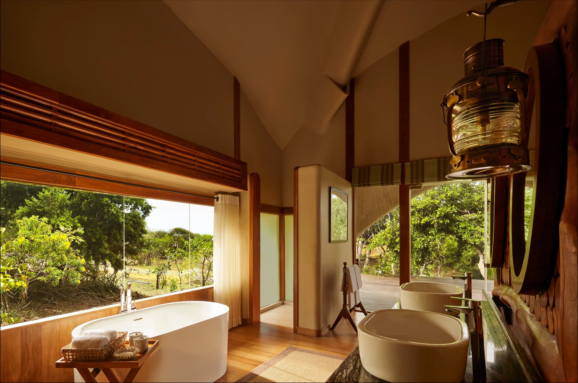 Cabin bathroom with a freestanding bathtub, stone basins and a window onto the bush