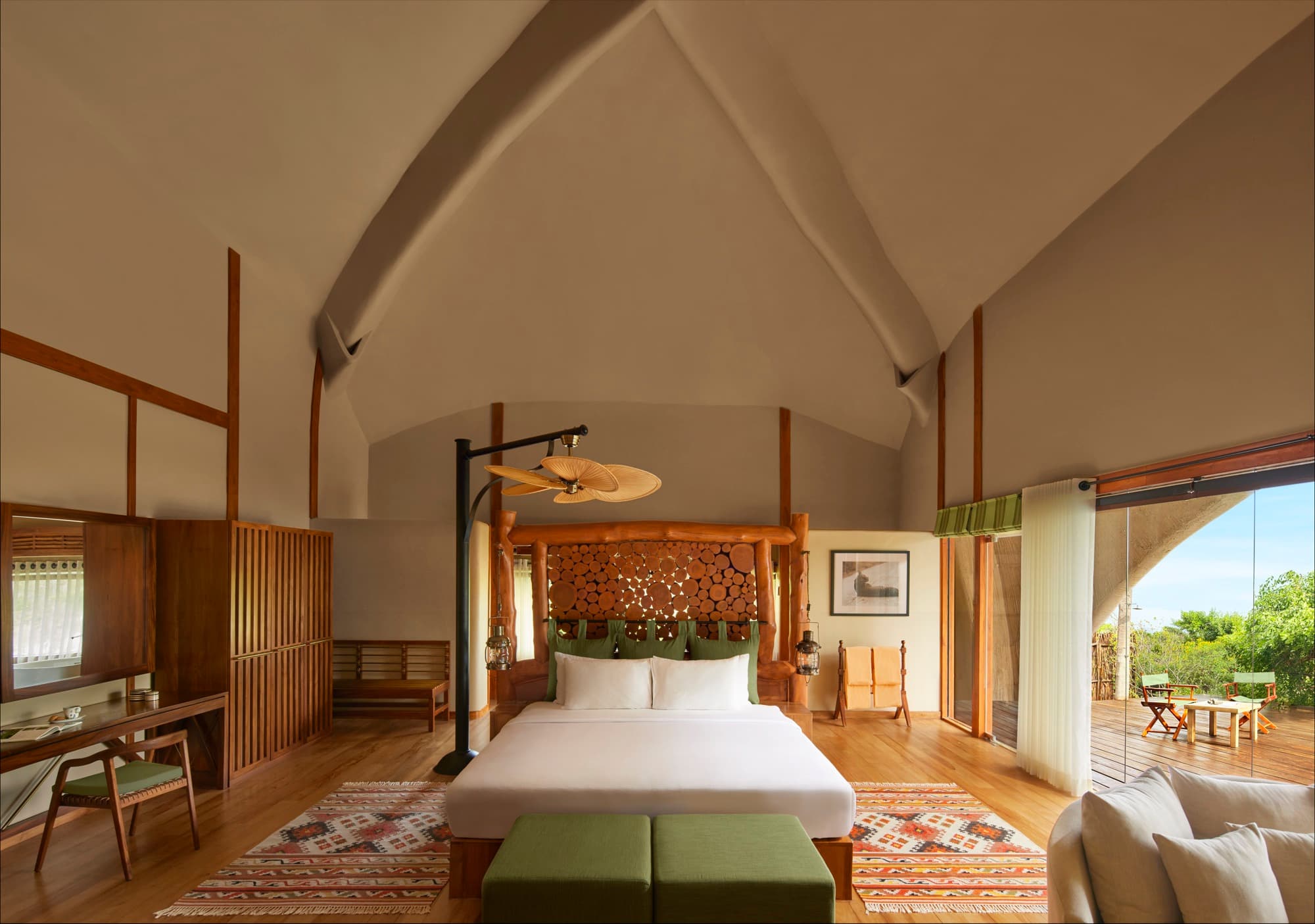 Cabin bedroom under a vaulted ceiling, with glass walls onto the bush