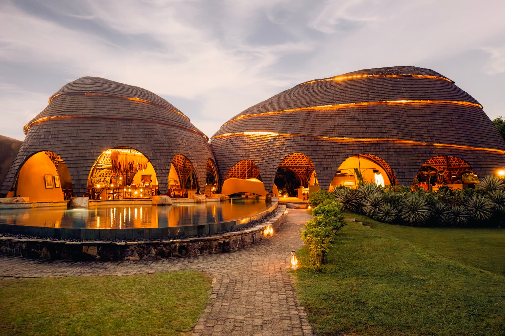 The bamboo and shingle pavilions lit at dusk, with the watering hole in the foreground