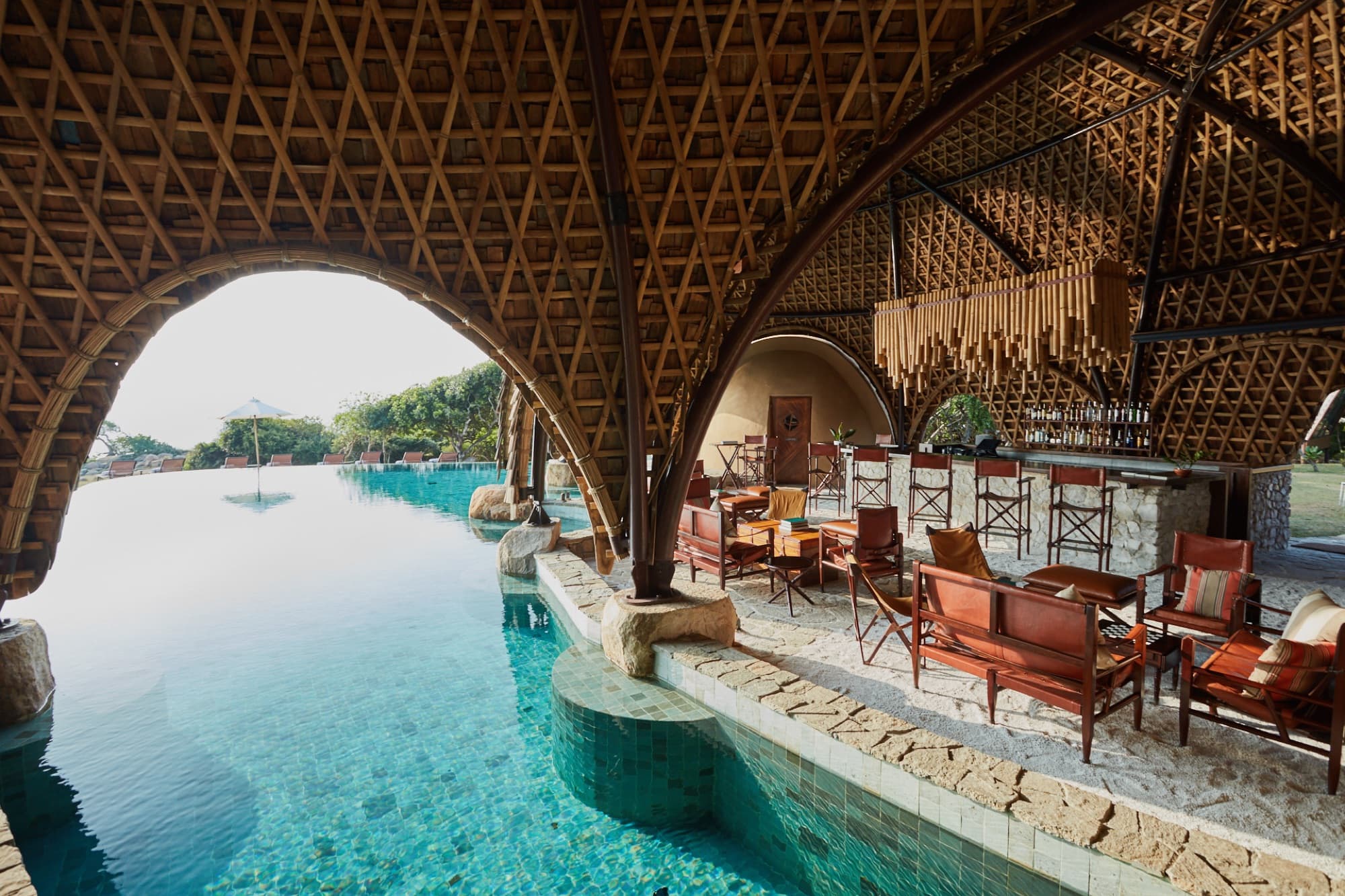 The pool bar under the woven bamboo vault, with leather safari chairs at the bar