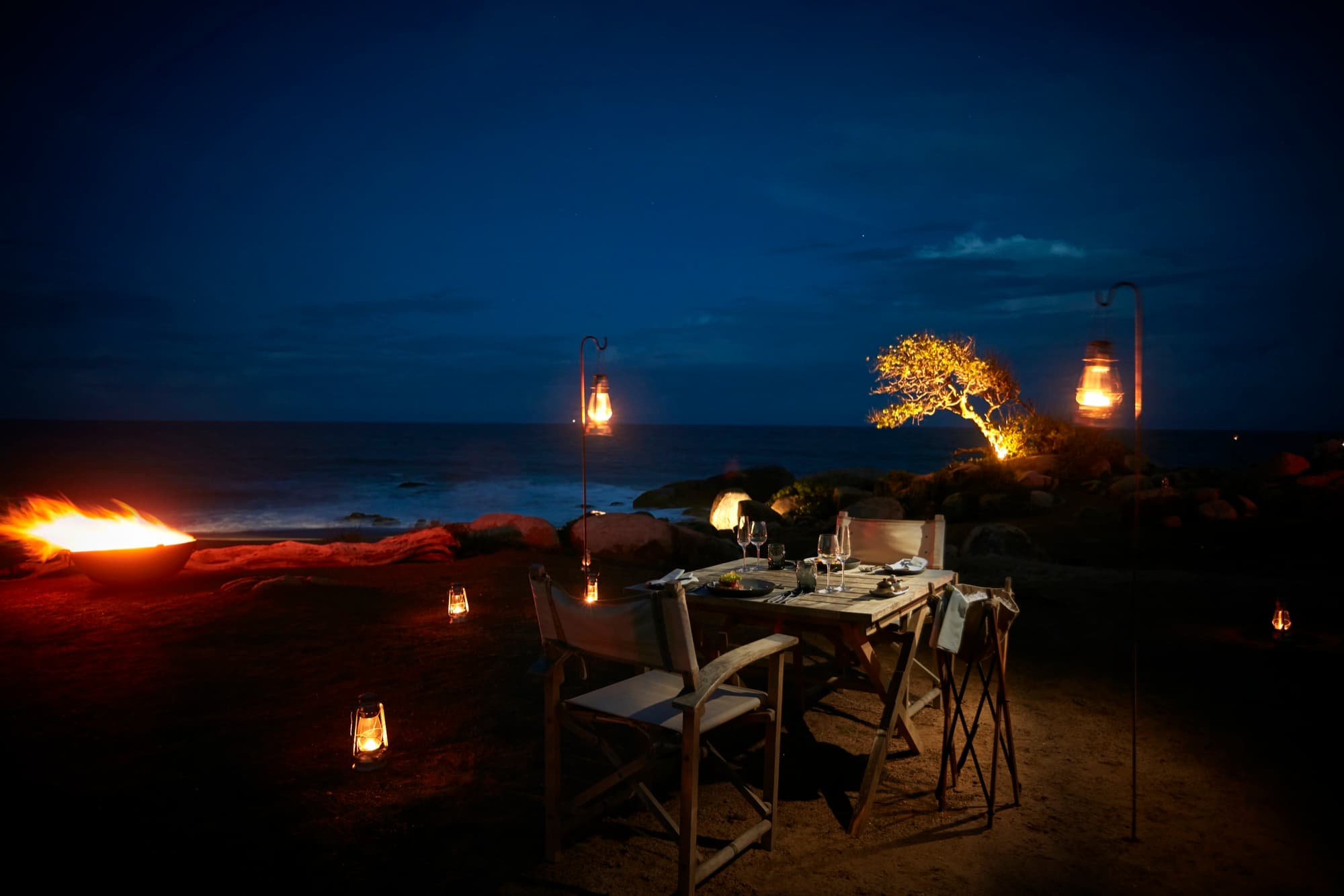 Wilderness dining set up at night by the rocks at the edge of the Indian Ocean