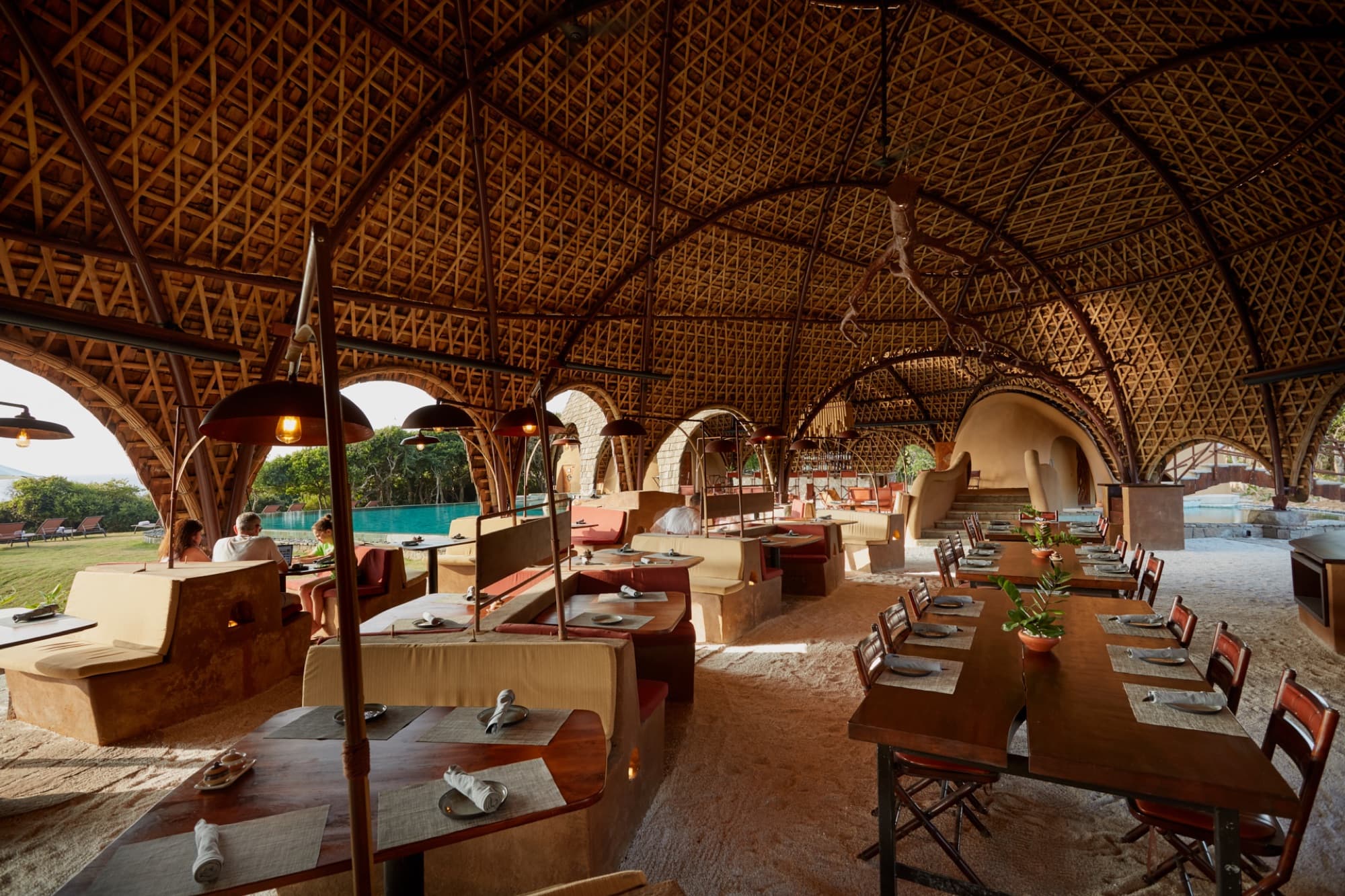 The open-air restaurant under a woven bamboo vault, with the pool seen through the arches