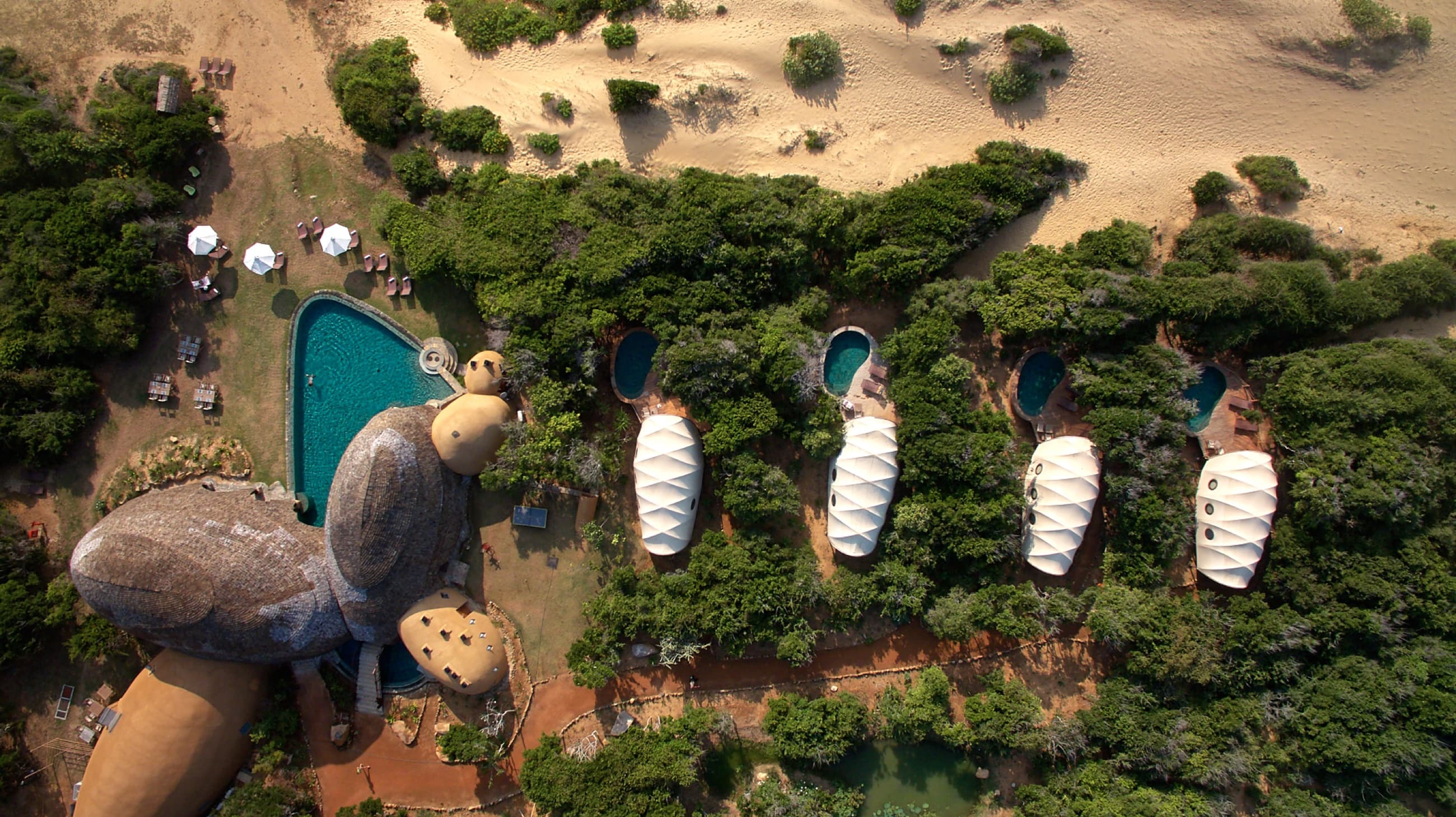 Aerial top-down view of four Cocoon tents aligned along the main pavilion and watering hole at Wild Coast Tented Lodge