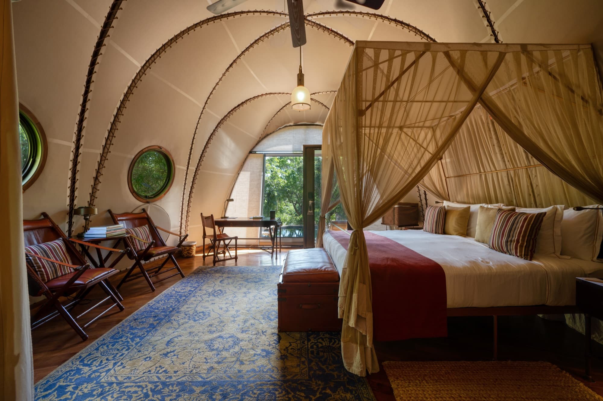 Wider view of a Cocoon Suite bedroom with vaulted ribbed canopy, porthole windows and a four-poster bed