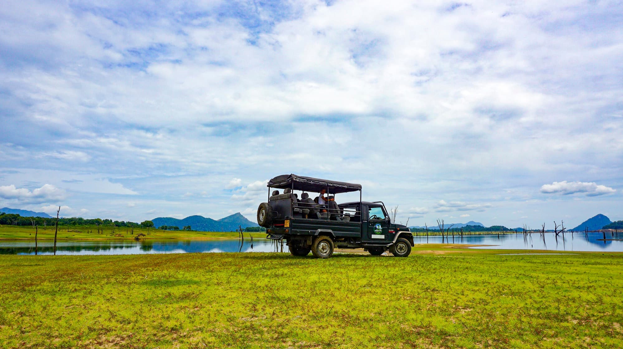 Safari jeep at the edge of a reservoir with mountains in the distance, on the Hathpotha safari