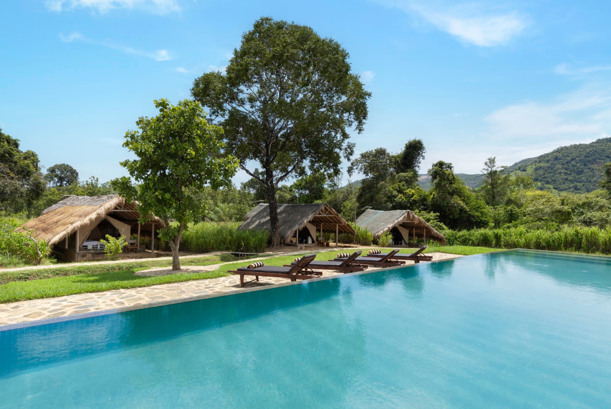 Infinity pool with lounge chairs facing the thatched tent pavilions and mountains