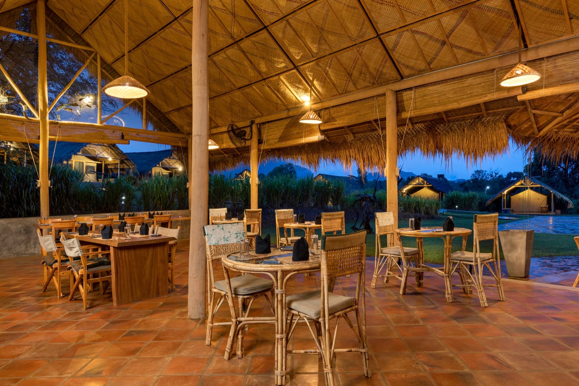 Main restaurant interior at dusk, lit lanterns under the thatched roof, tents visible outside
