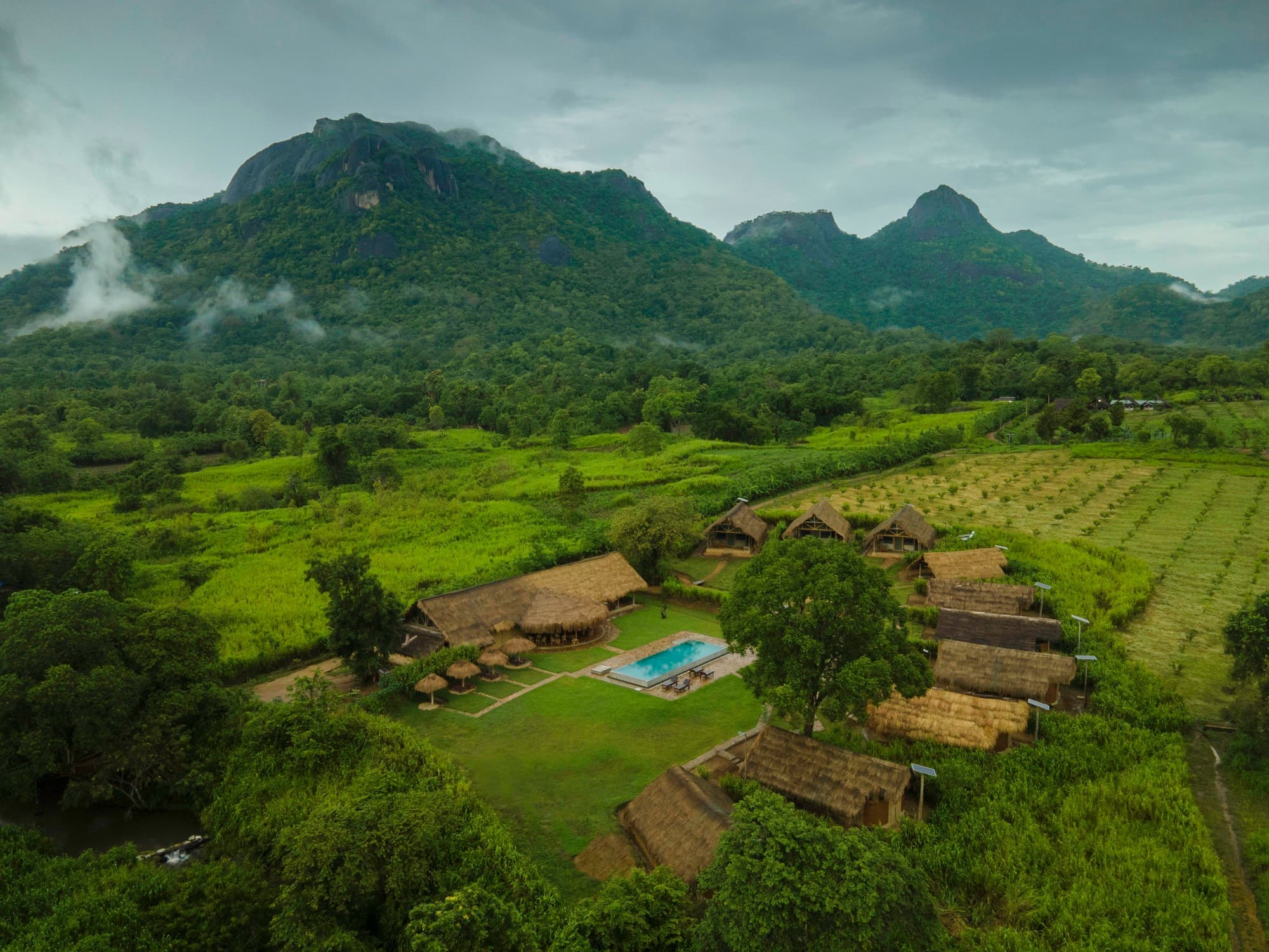 Wide aerial view of the property in a green valley with mist-wrapped mountains behind