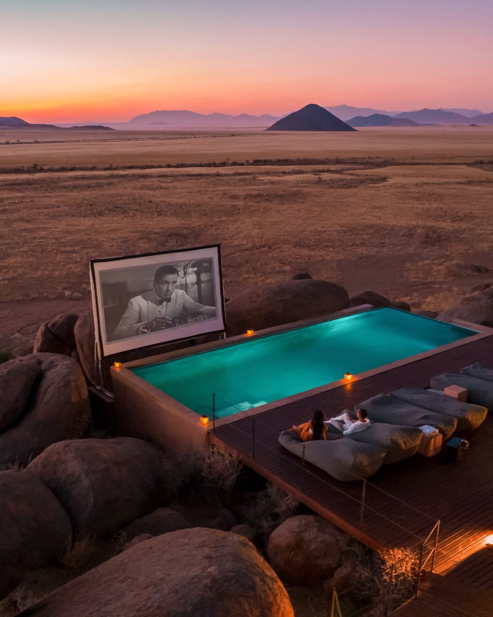 Outdoor cinema screen beside the infinity pool, among the boulders at sunset