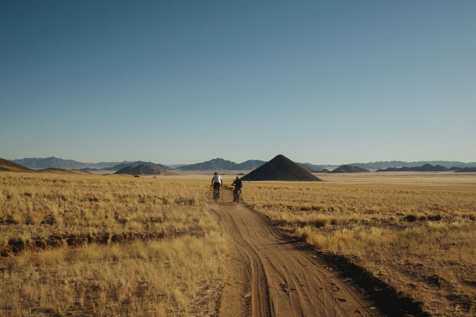 Two cyclists on a sand track through golden grass