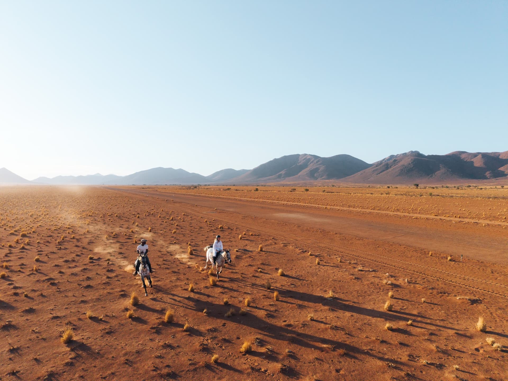 Two riders crossing the red sand, seen from above