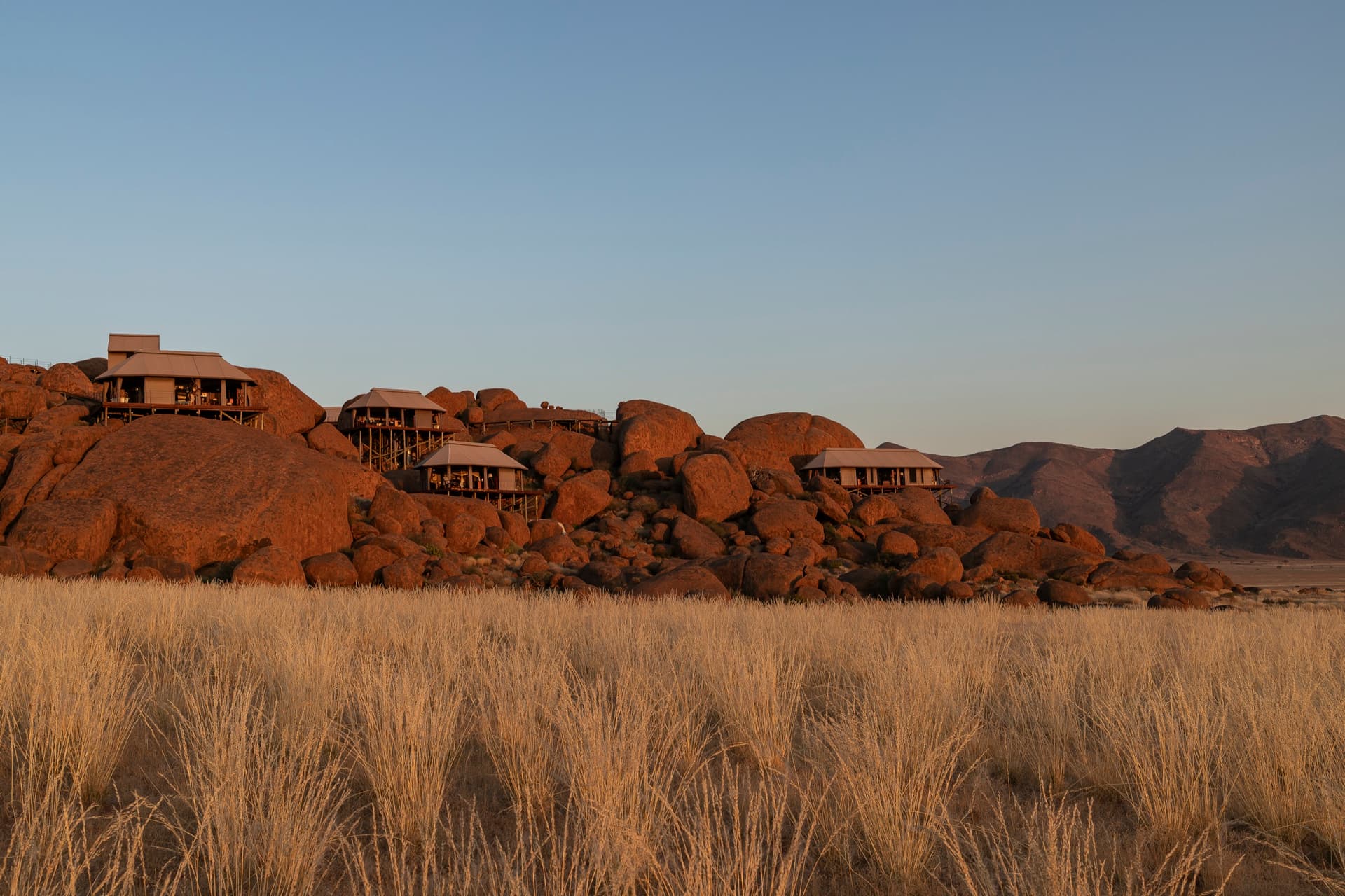 Tents on stilts among granite boulders above golden grass — Zannier Sonop, southern Namib Desert, Namibia