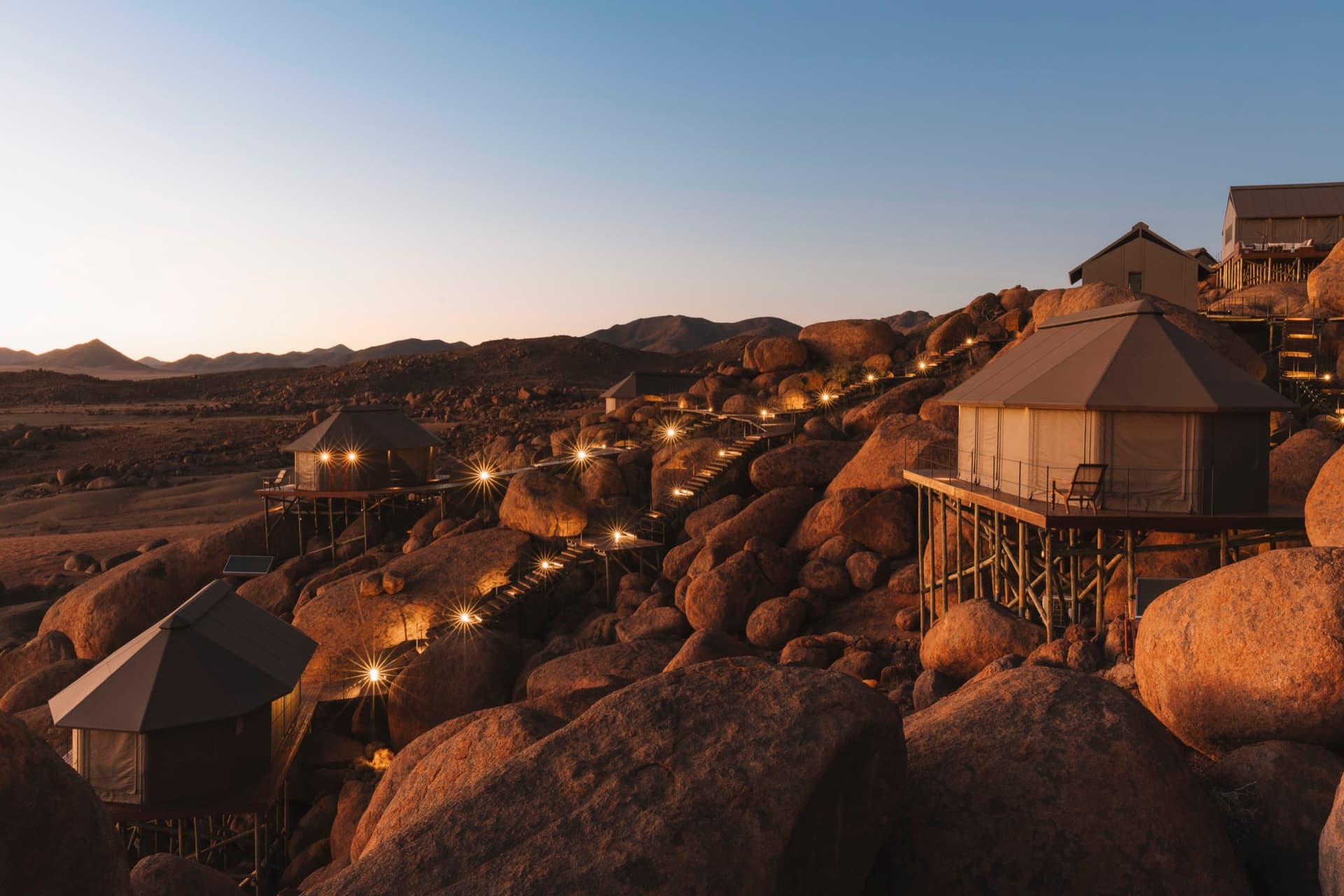 Tents on stilts lit up among the boulders at dusk