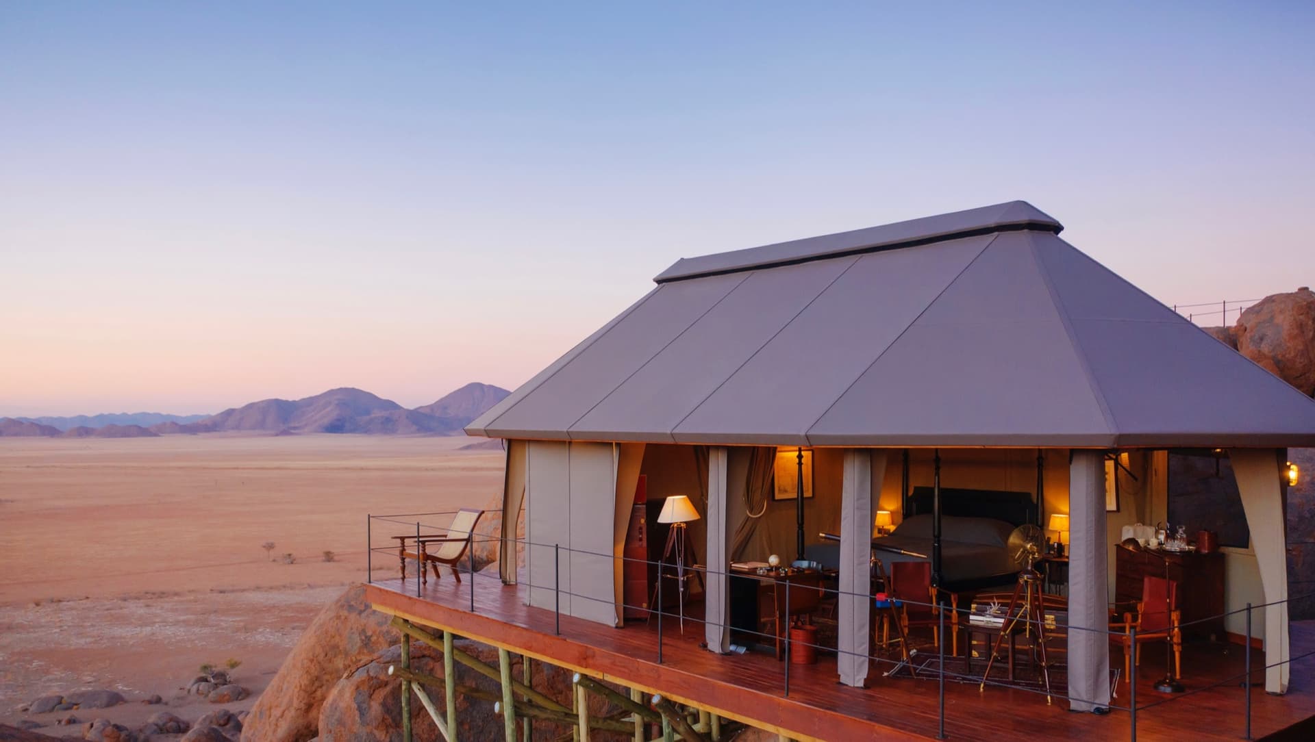 A tent on stilts at the edge of the boulders, open to the desert at dusk