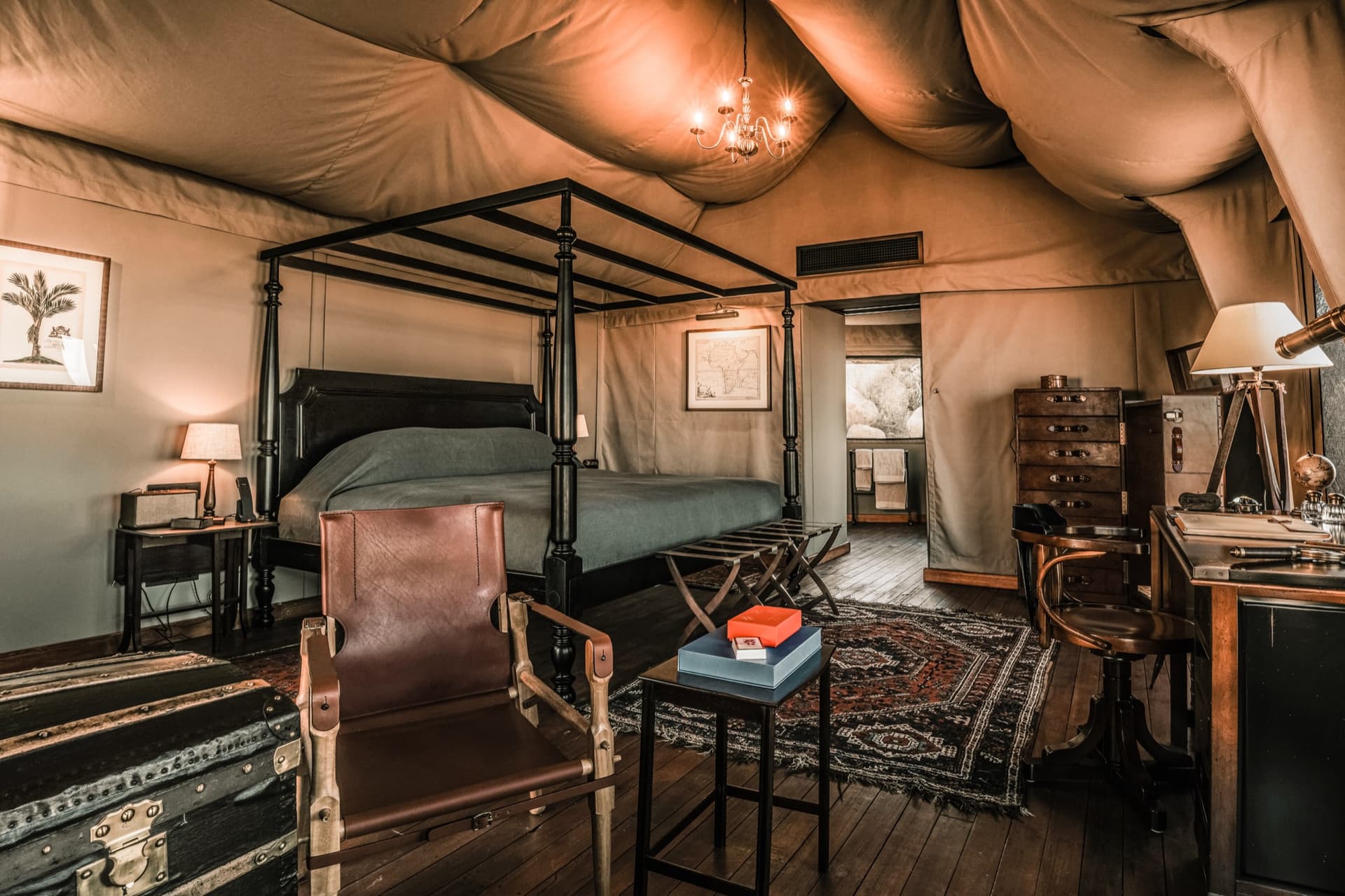 Four-poster bed and leather armchair under the canvas of a tent