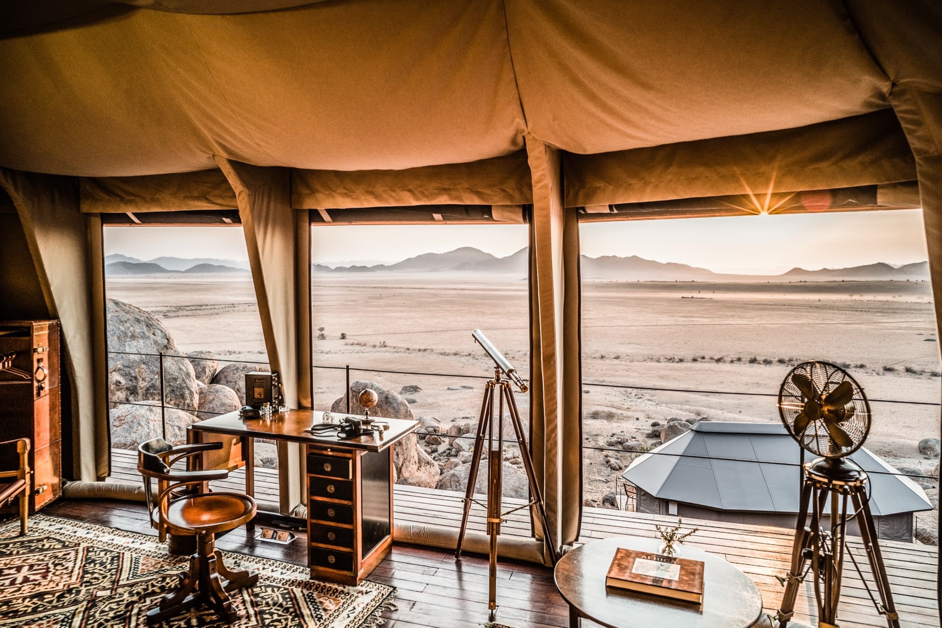 Writing desk, telescope and antiques in a tent facing the desert plains at sunrise