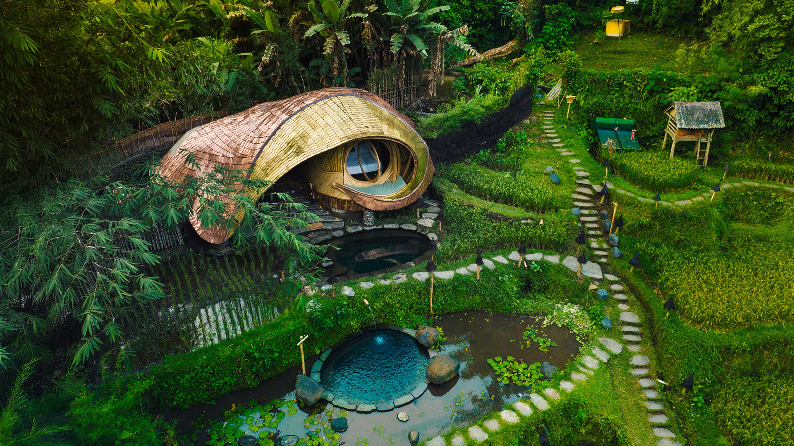 Aerial view of a bamboo house with round spring-fed plunge pools among rice terraces — Bambu Indah, Sayan Ridge near Ubud, Bali