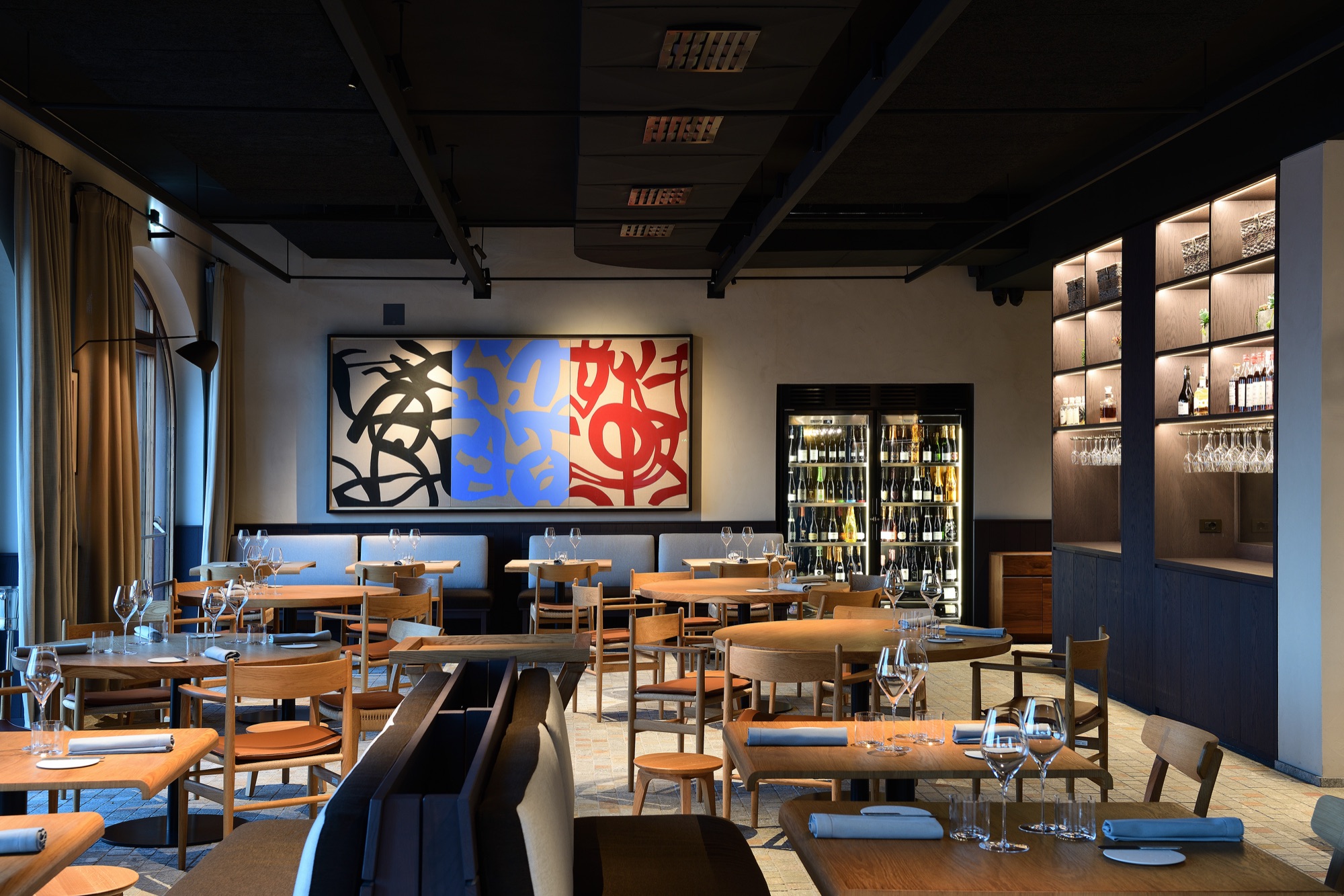 Dining room of Fàula restaurant, with a large colourful painting and a wine wall