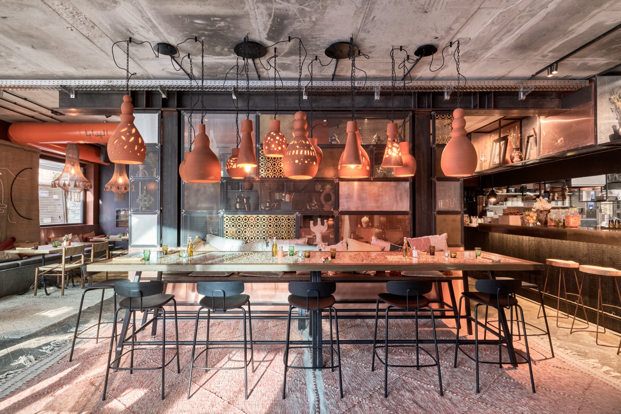 Restaurant with a long shared table under copper pendant lamps, next to the bar
