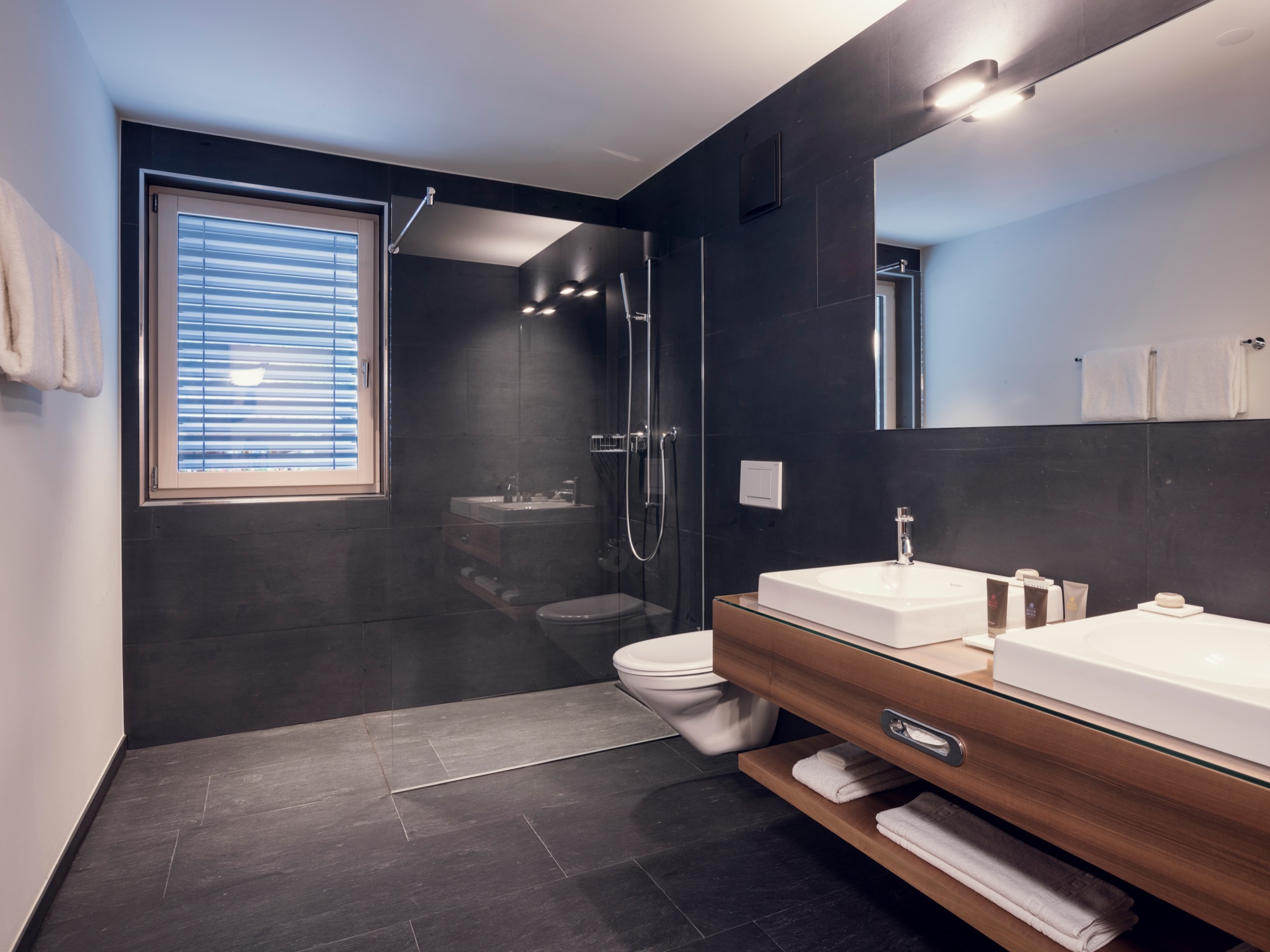 Bathroom in dark tiles with a double washbasin on a wooden unit