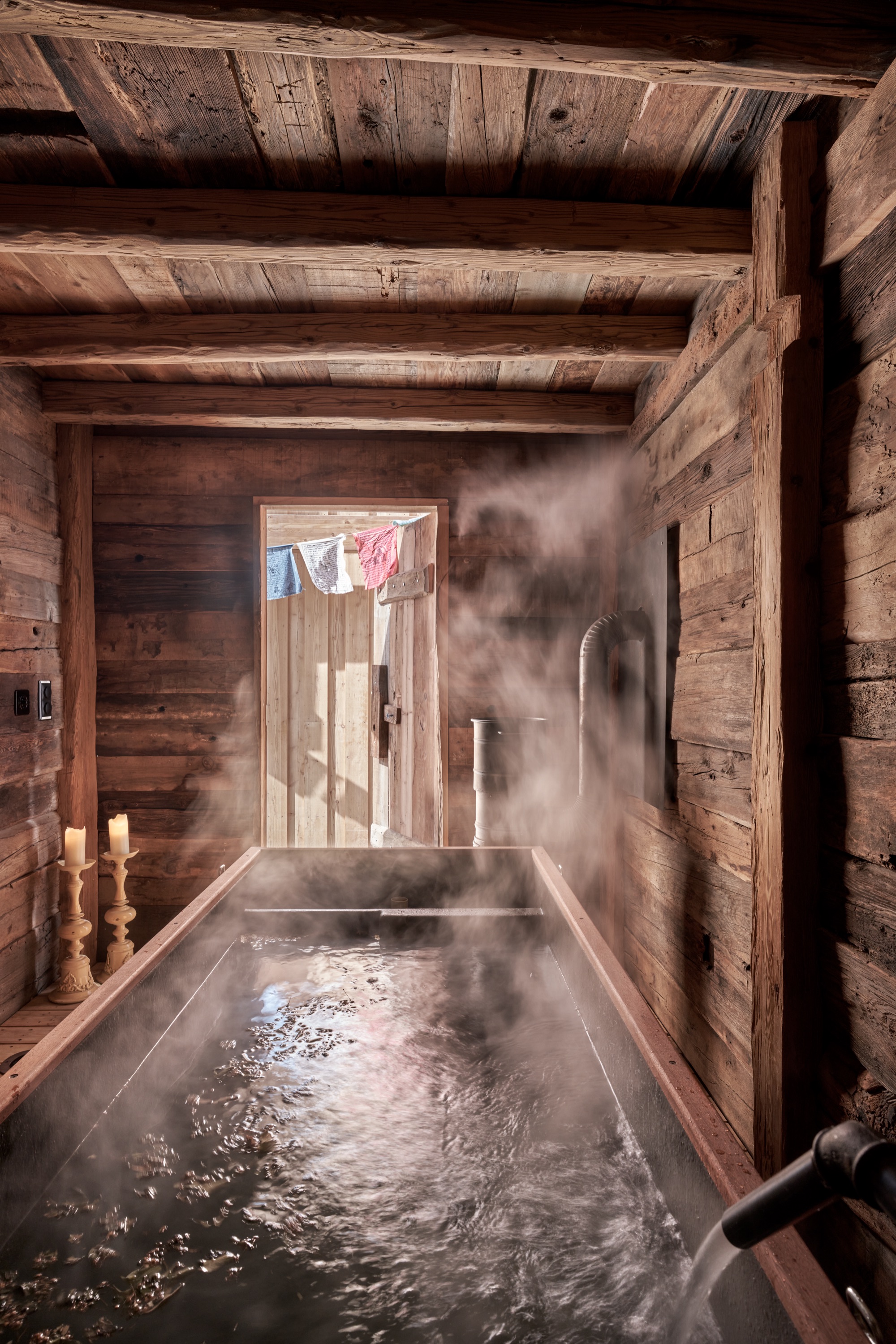 Steam rising from a wooden bath in a candlelit timber room