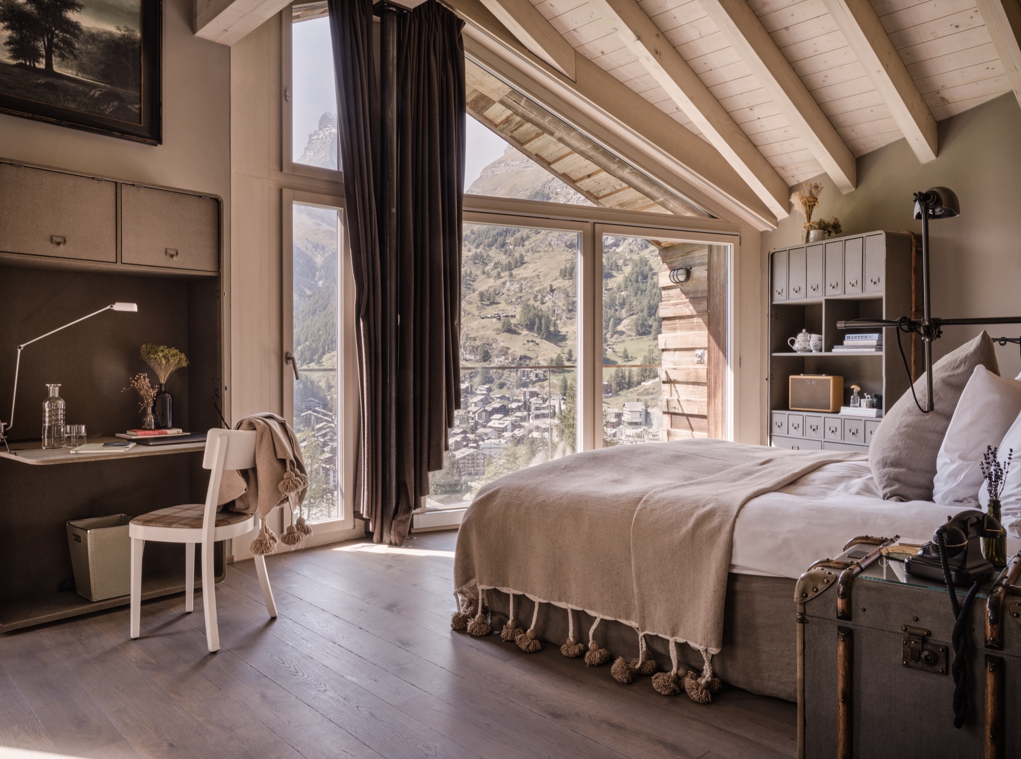 Bedroom under a beamed roof, with a desk and a tall window onto the valley