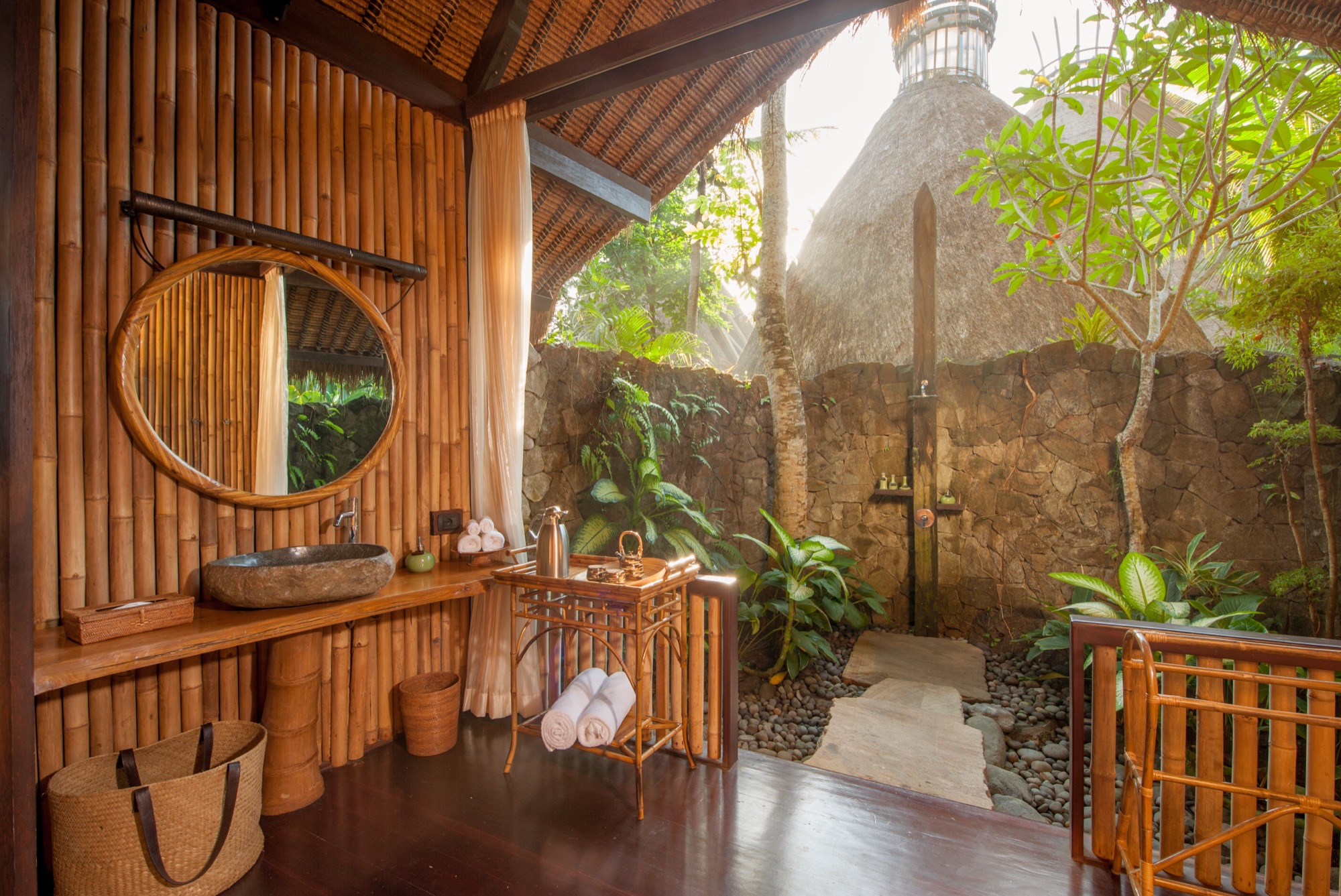 Outdoor bathroom with bamboo wall, stone shower and round mirror