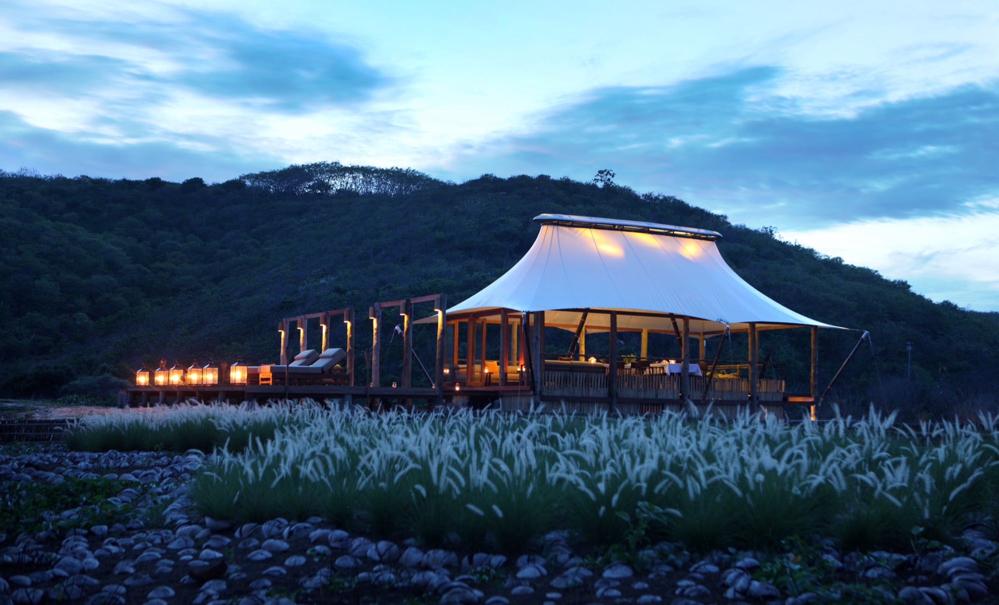 Dermaga restaurant terrace in the evening — open deck, fire pit seating and thatched pavilion
