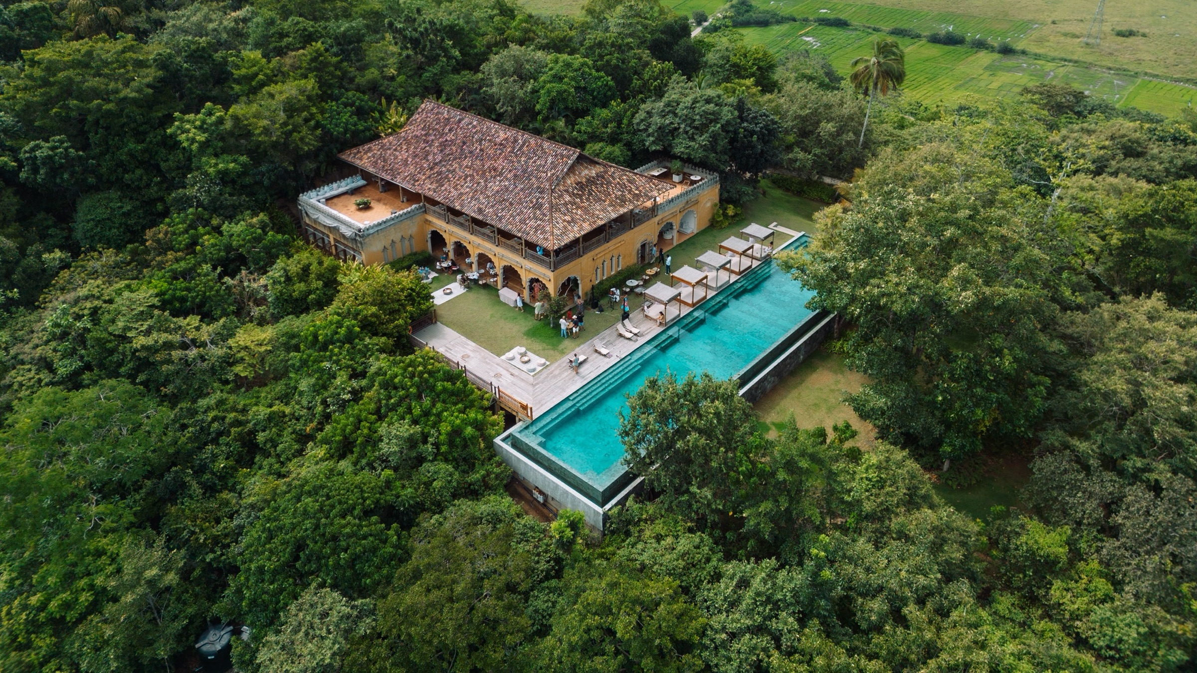 Aerial view of the Main House and 35-metre infinity pool on the forested hilltop, paddy fields beyond — Malabar Hill, near Weligama, Sri Lanka