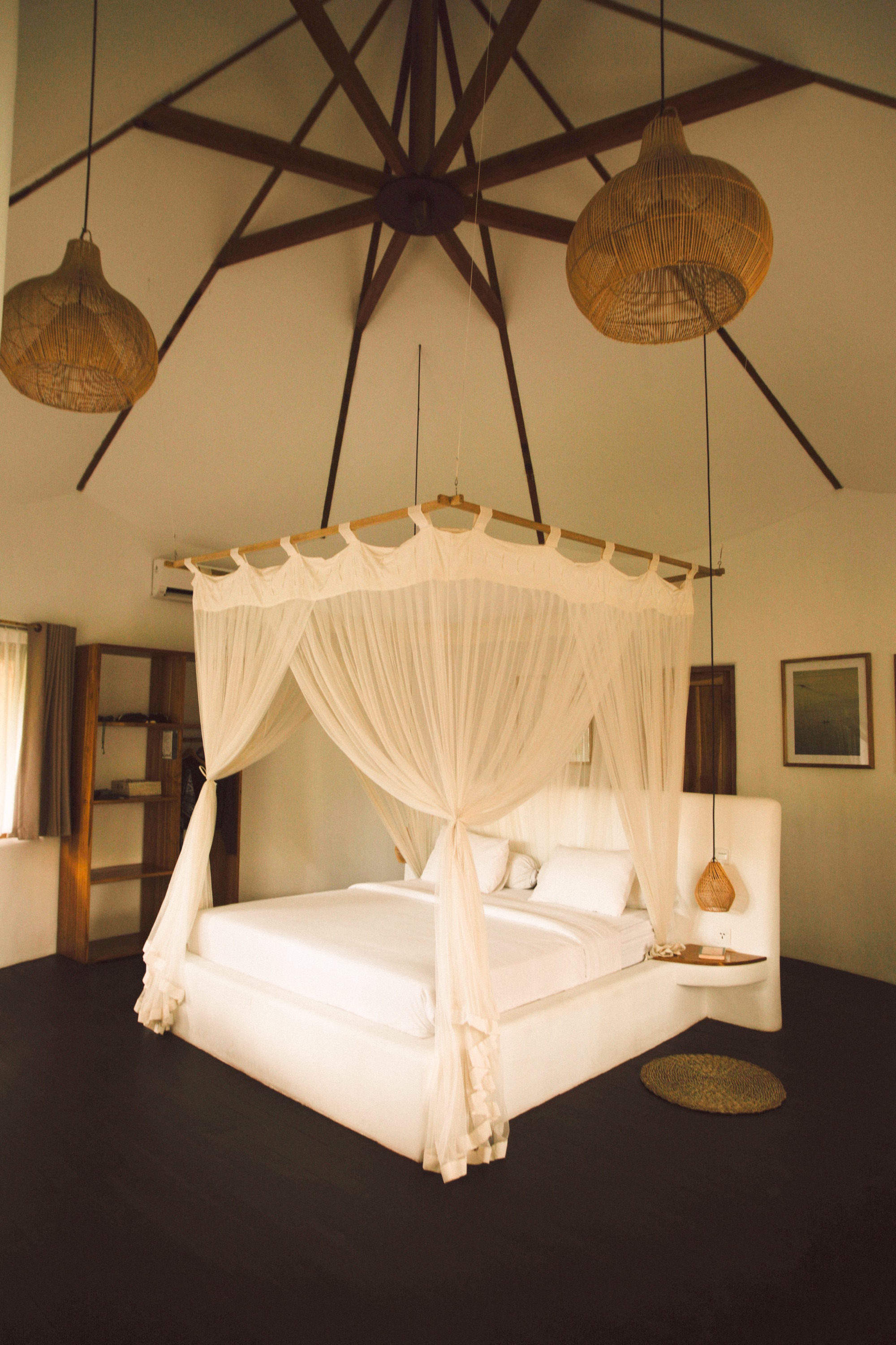 Canopy bed under a high vaulted ceiling with woven rattan pendant lamps