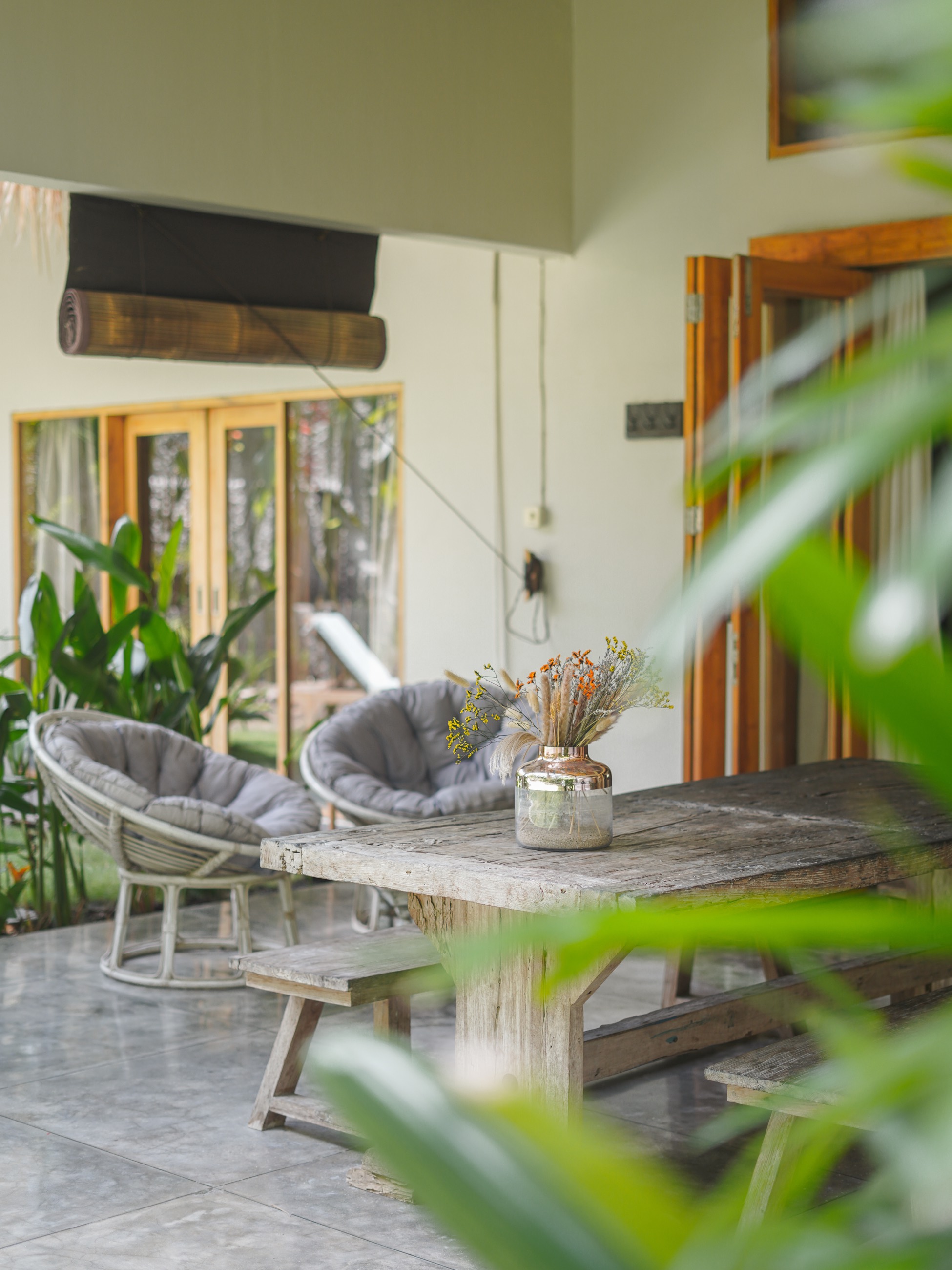 Covered villa terrace with grey papasan chairs and a weathered timber table