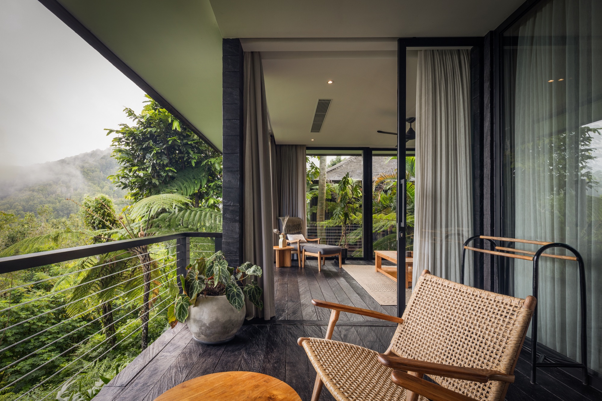 Cabin balcony with rattan chairs facing forested mountains wrapped in mist