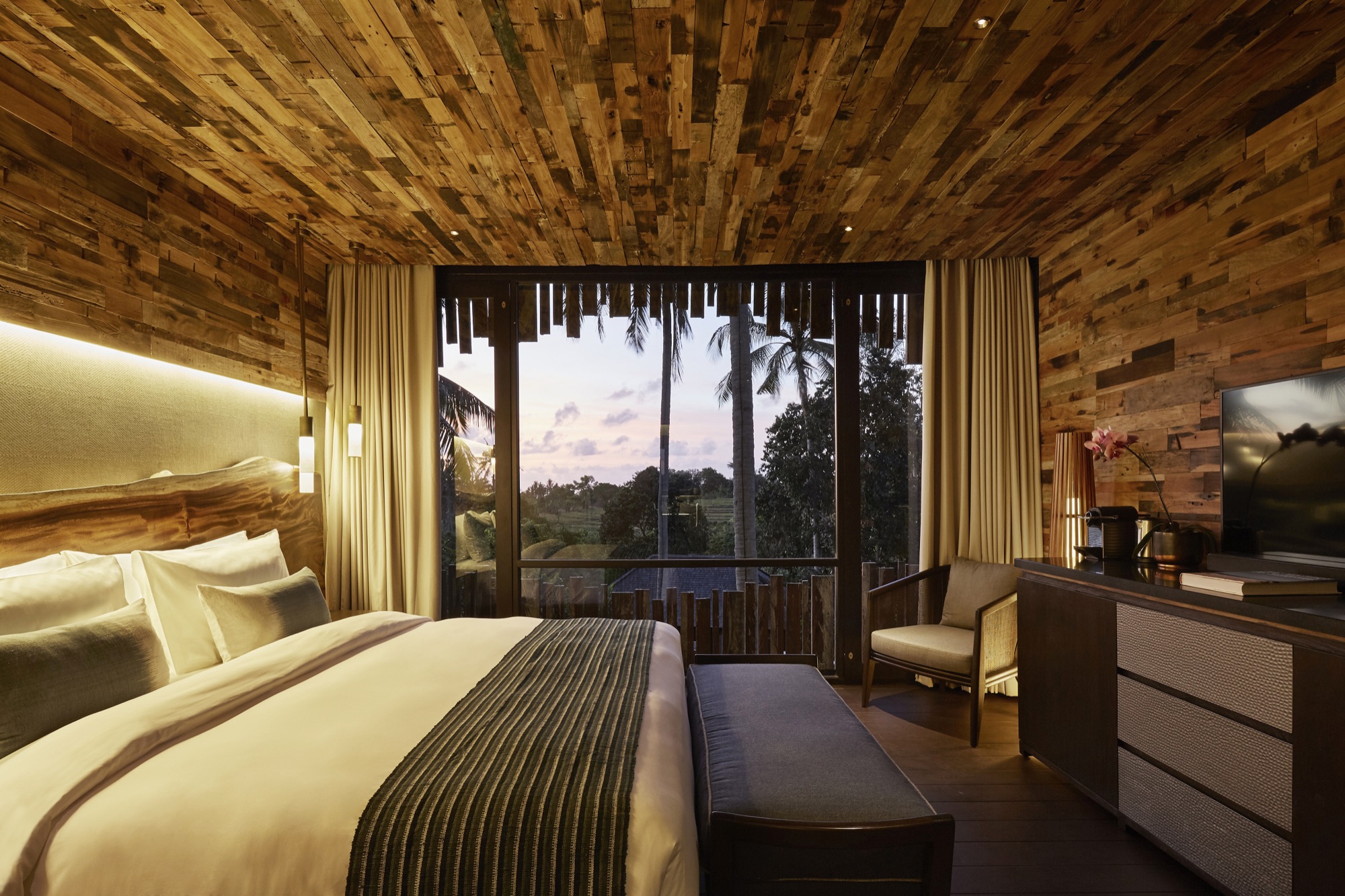Canopy Suite bedroom with timber walls opening to rice fields at dusk