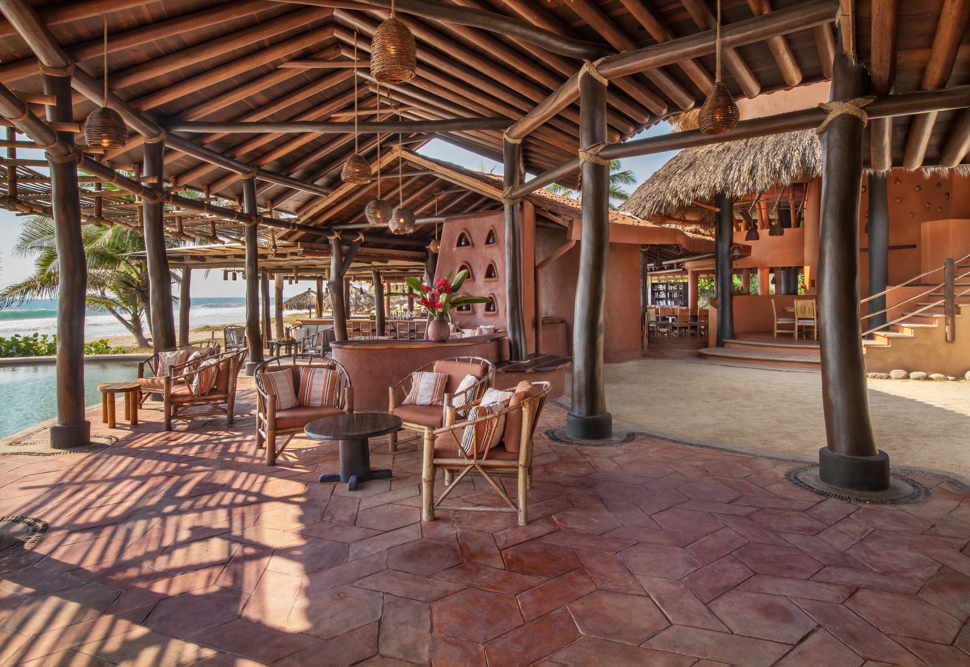 Open-air lounge with sofas under a timber roof, the sea beyond