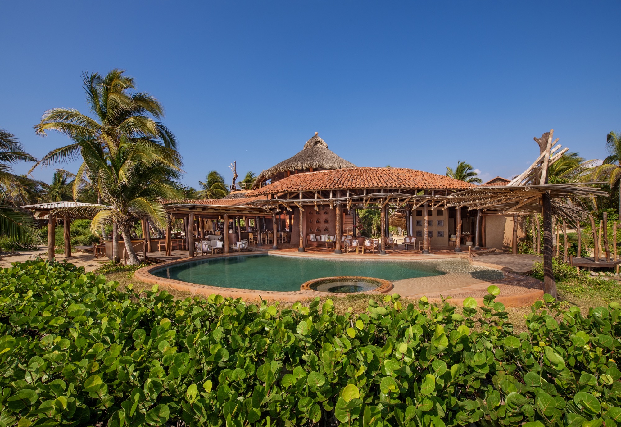 Pool and main building with a tiled roof, framed by palms