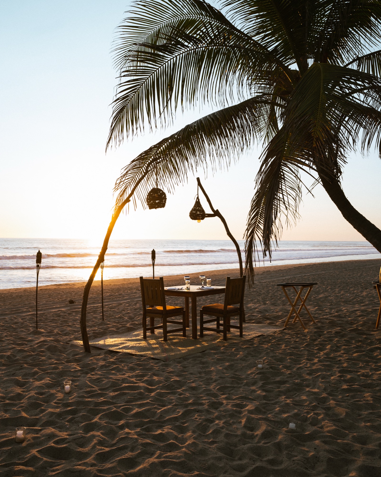 Table set on the sand at sunset, with lanterns