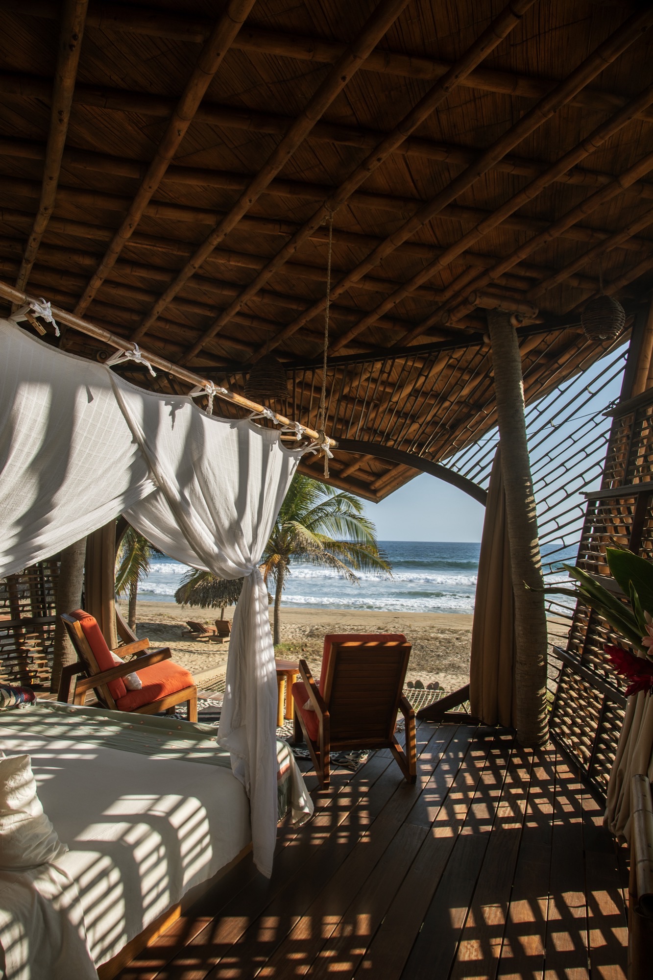 Mosquito-net bed and armchairs in a Manta treehouse, the sea in the background