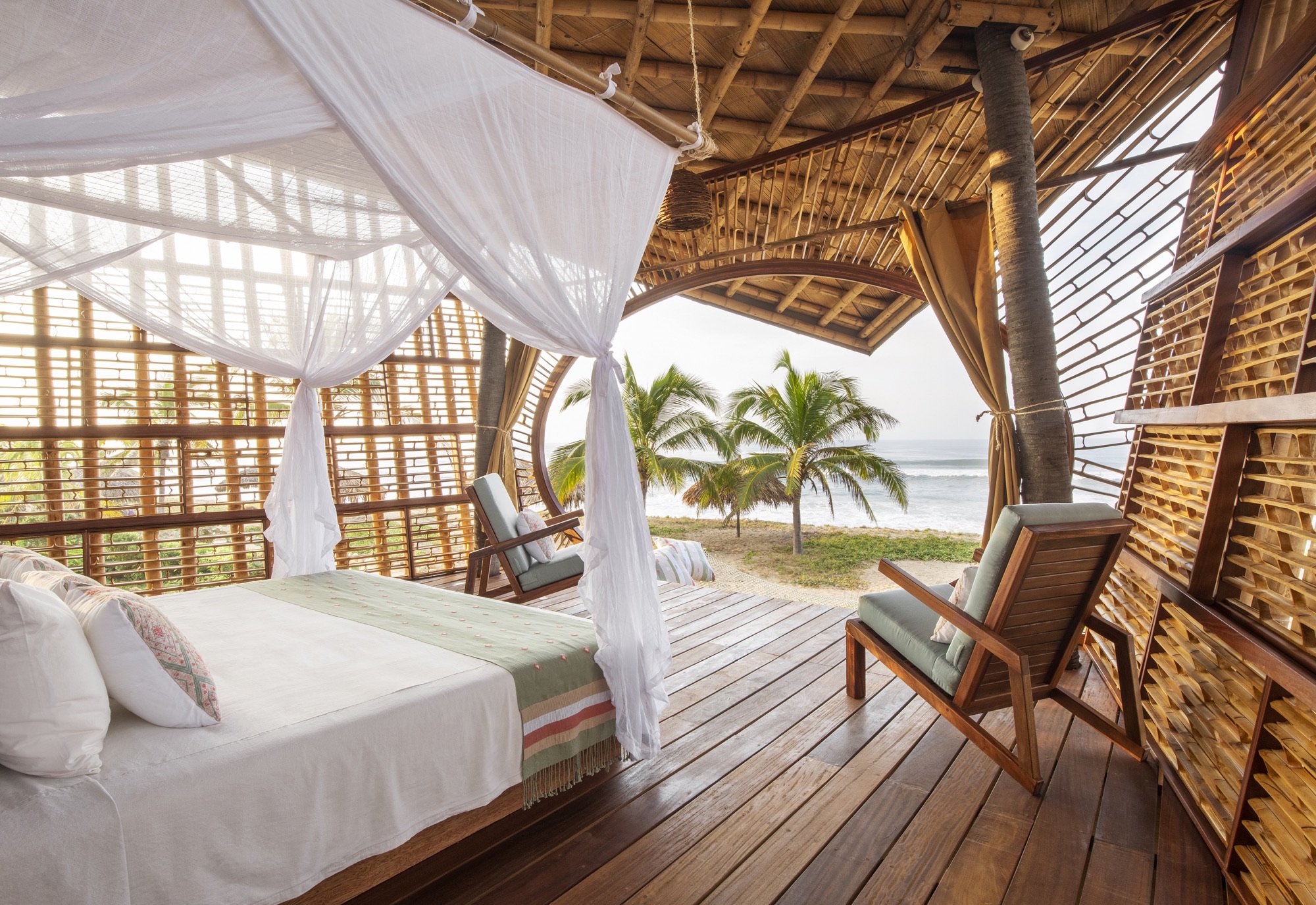 Bed under a mosquito net in a bamboo Manta treehouse, open to the beach